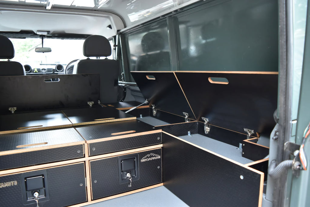 Black storage compartments in a Defender 110 Utility interior with visible branding of Hexamoto