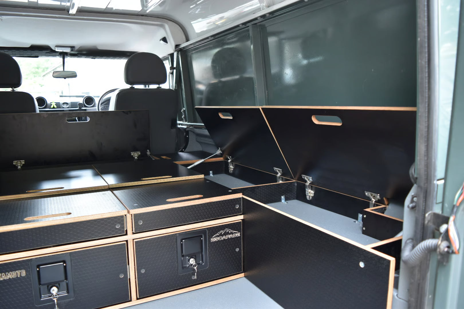 Black storage compartments in a Defender 110 Utility interior with visible branding of Hexamoto