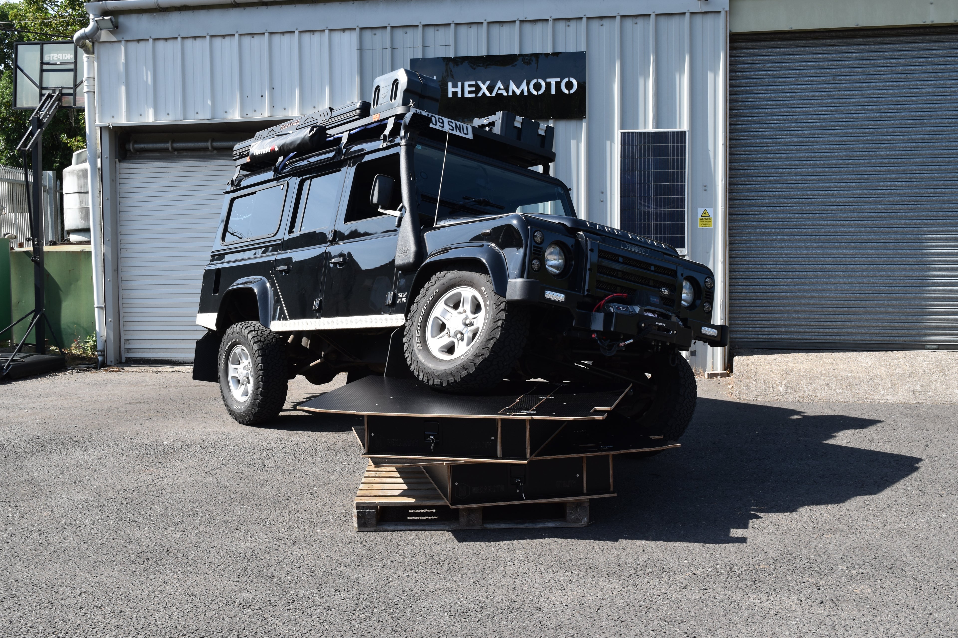 Defender off roading vehicle parked on two Defender Utility storage systems by Hexamoto to show the strength of the product. 