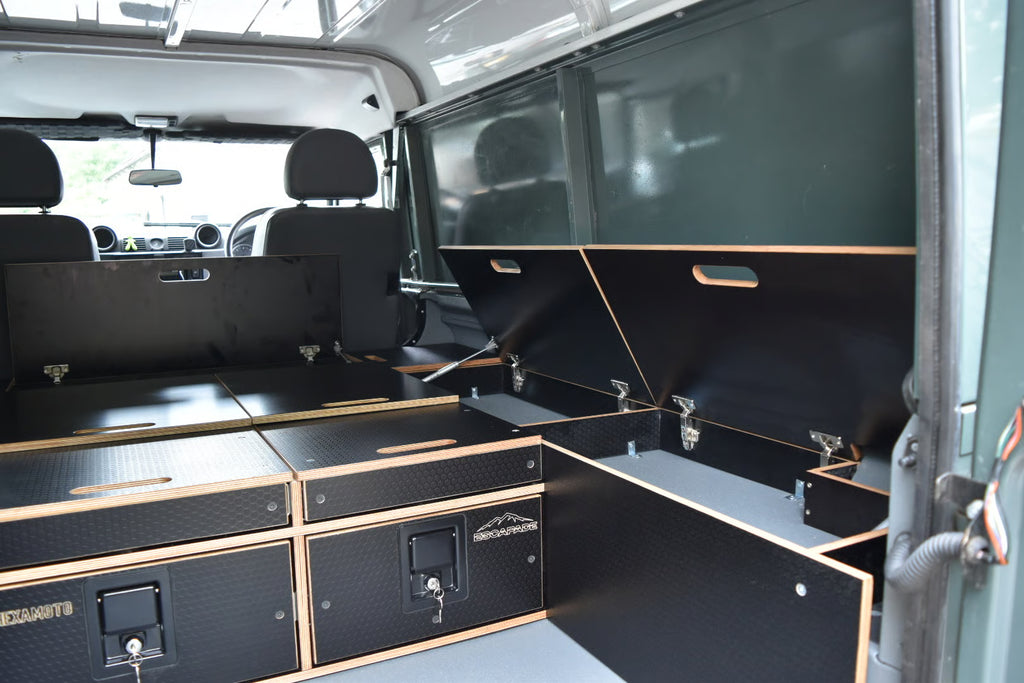 Black storage compartments and cabinets inside a Defender, with 'Hexamoto' branding.