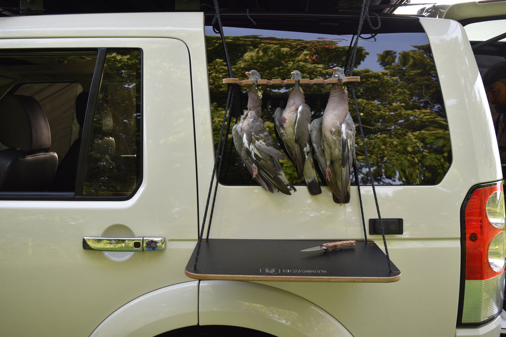 Pigeons hanging from a bird hanger mounted to a car with a table underneath with a knife led on the table