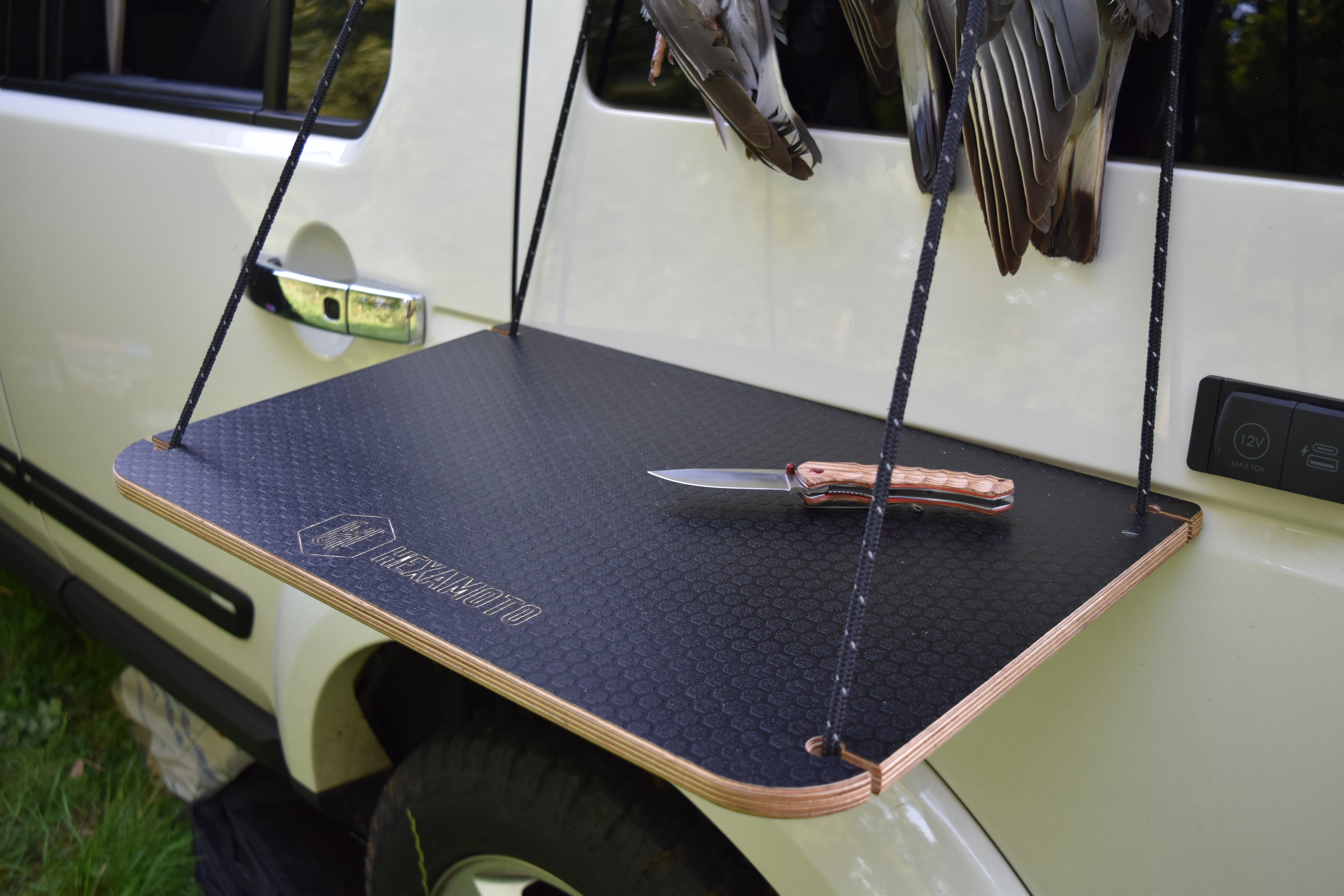 Black table with a knife on a vehicle's rear quarter, with birds hanging above