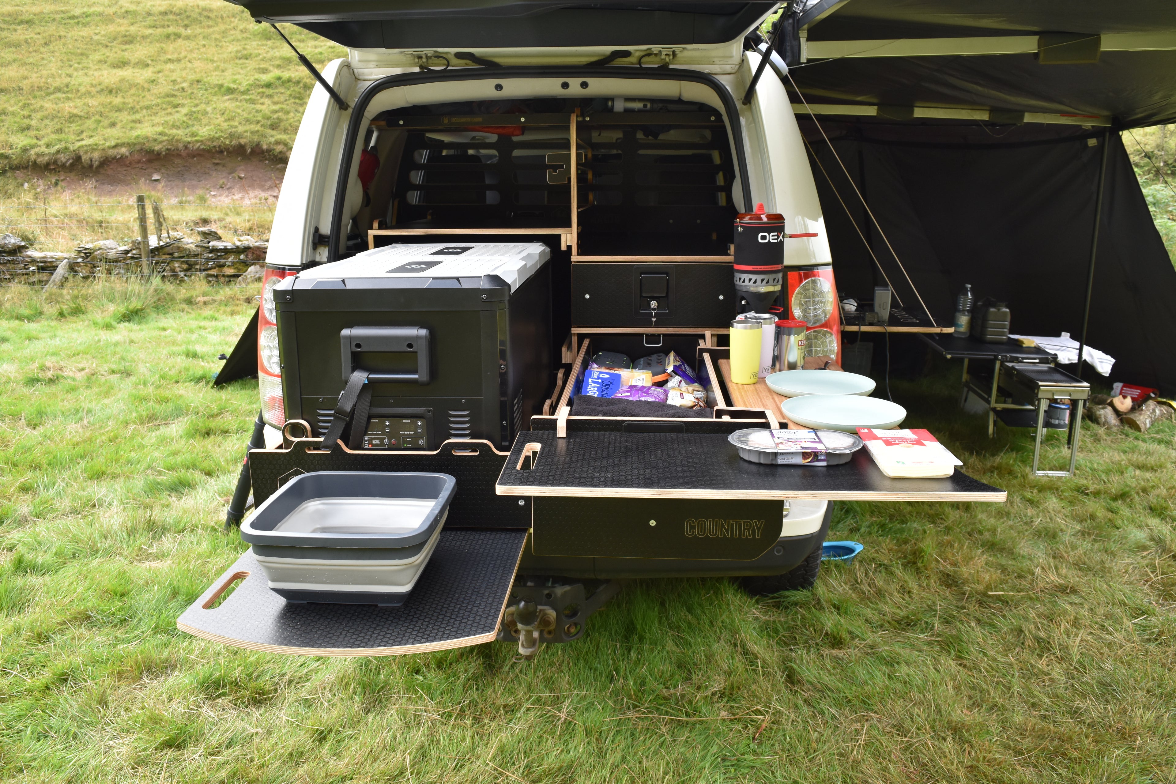 Land Rover Discovery 4 with open cargo area displaying camping gear and supplies on a grassy field.
