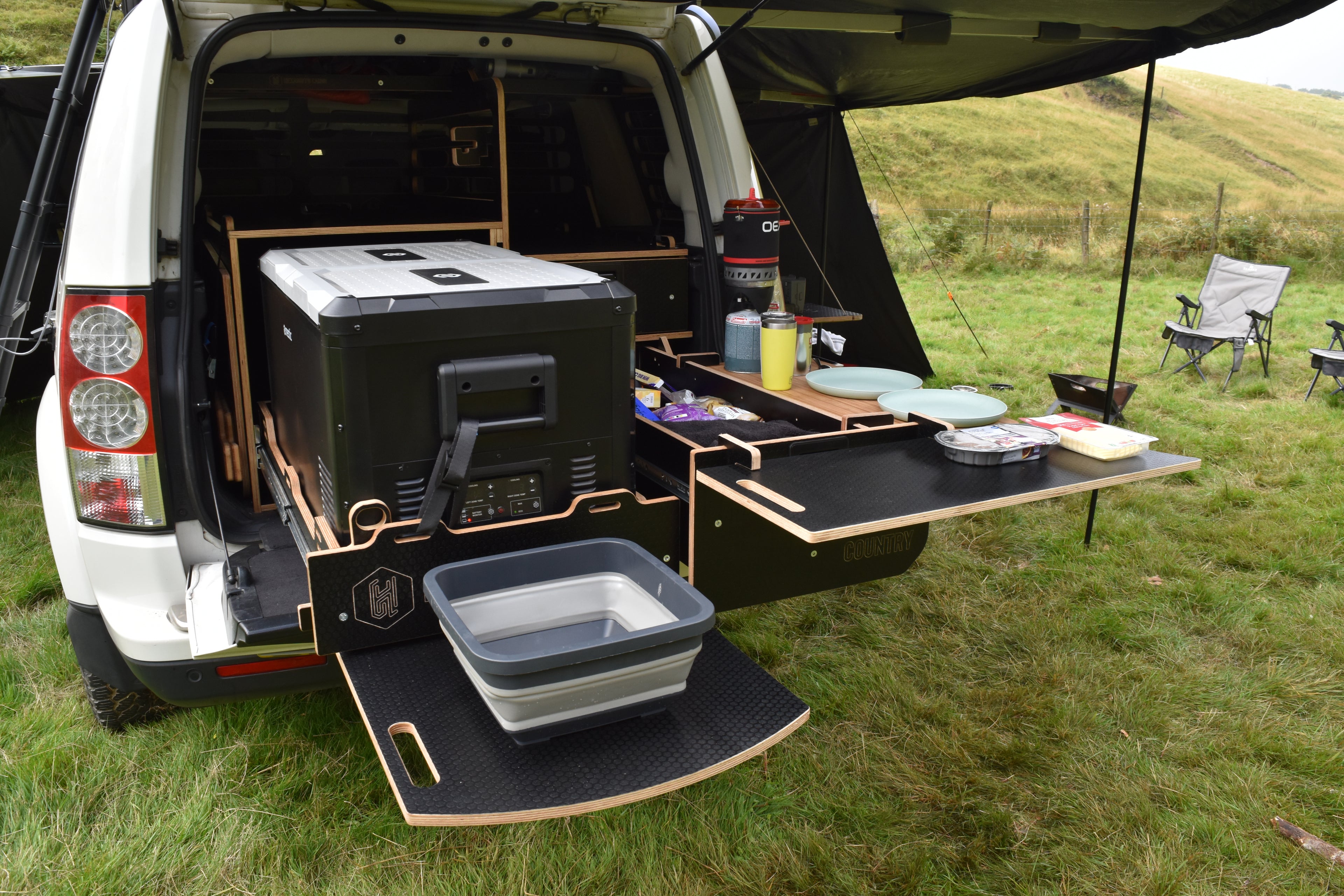 Vehicle with open cargo area set up for camping in a grassy outdoor setting