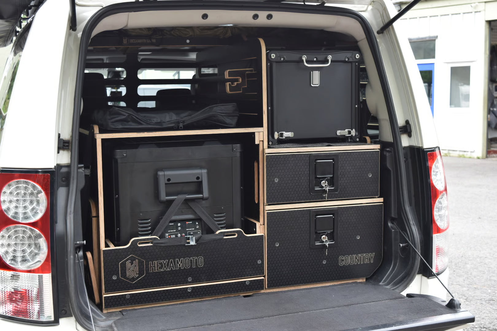 Back of a van with black storage drawers labeled 'HEXAMOTO' brand, arranged inside.