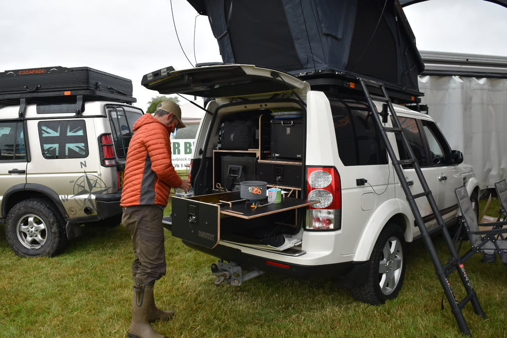 Person preparing a vehicle with camping gear in an outdoor setting