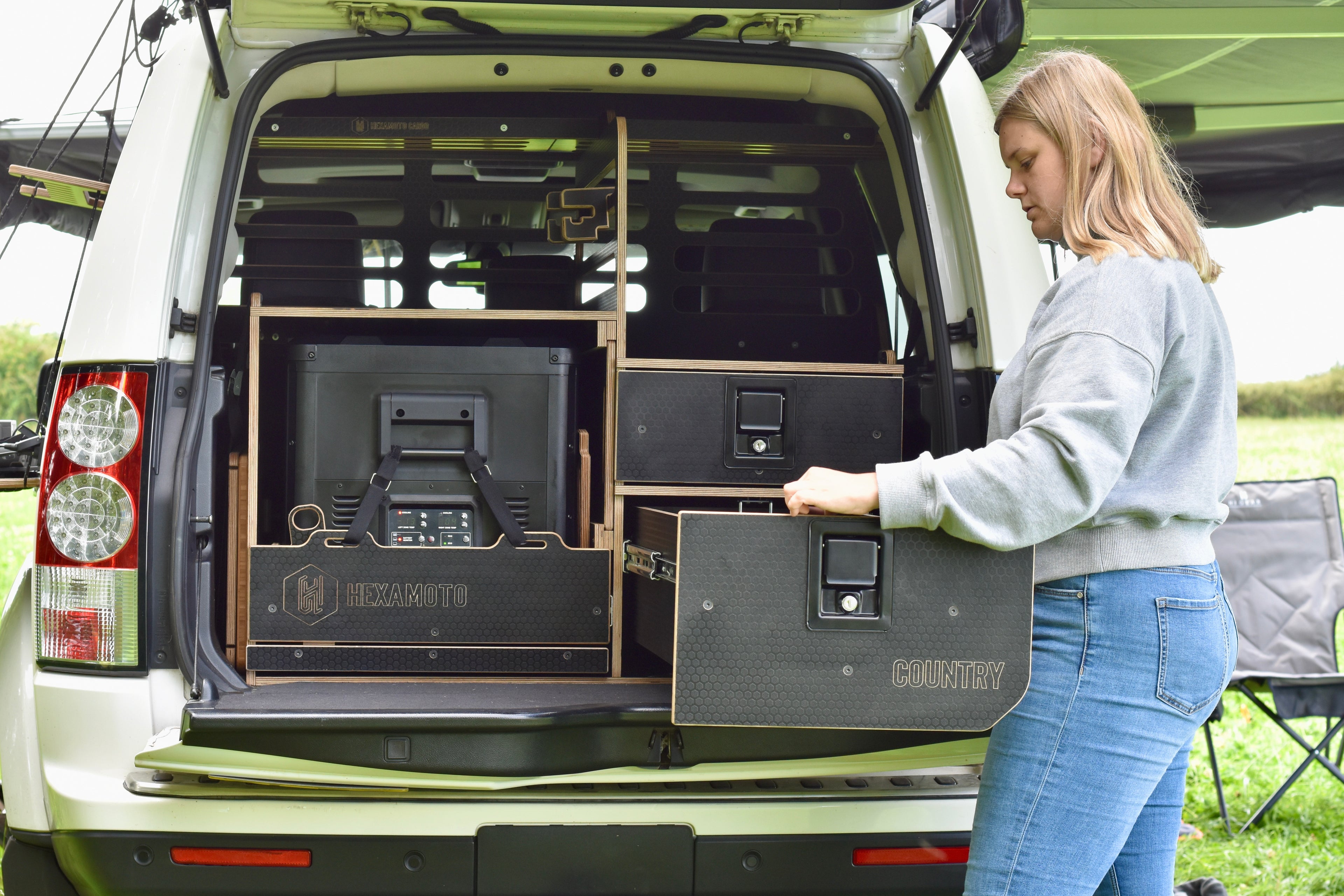 Person setting up a camping setup in the back of a vehicle with a coolbox