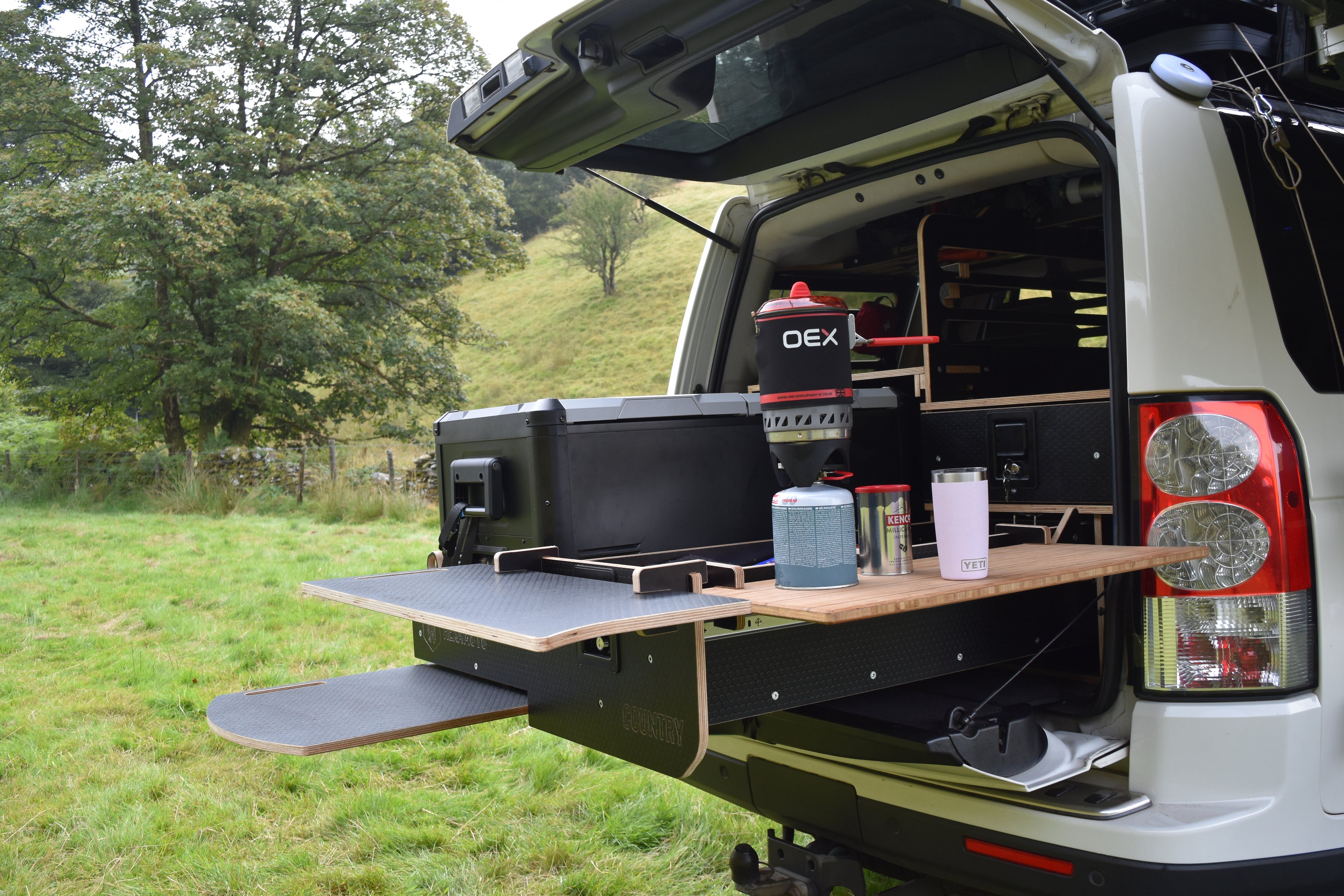 Trunk of a vehicle with an open cargo area displaying camping gear and a table.