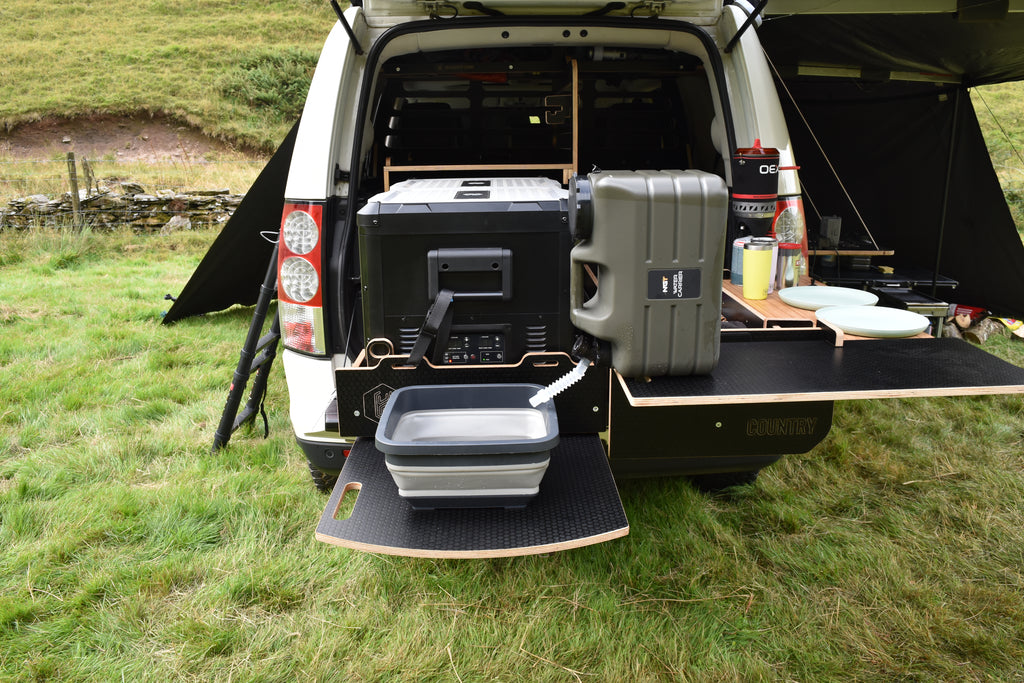 Vehicle with open cargo area set up for camping on a grassy field