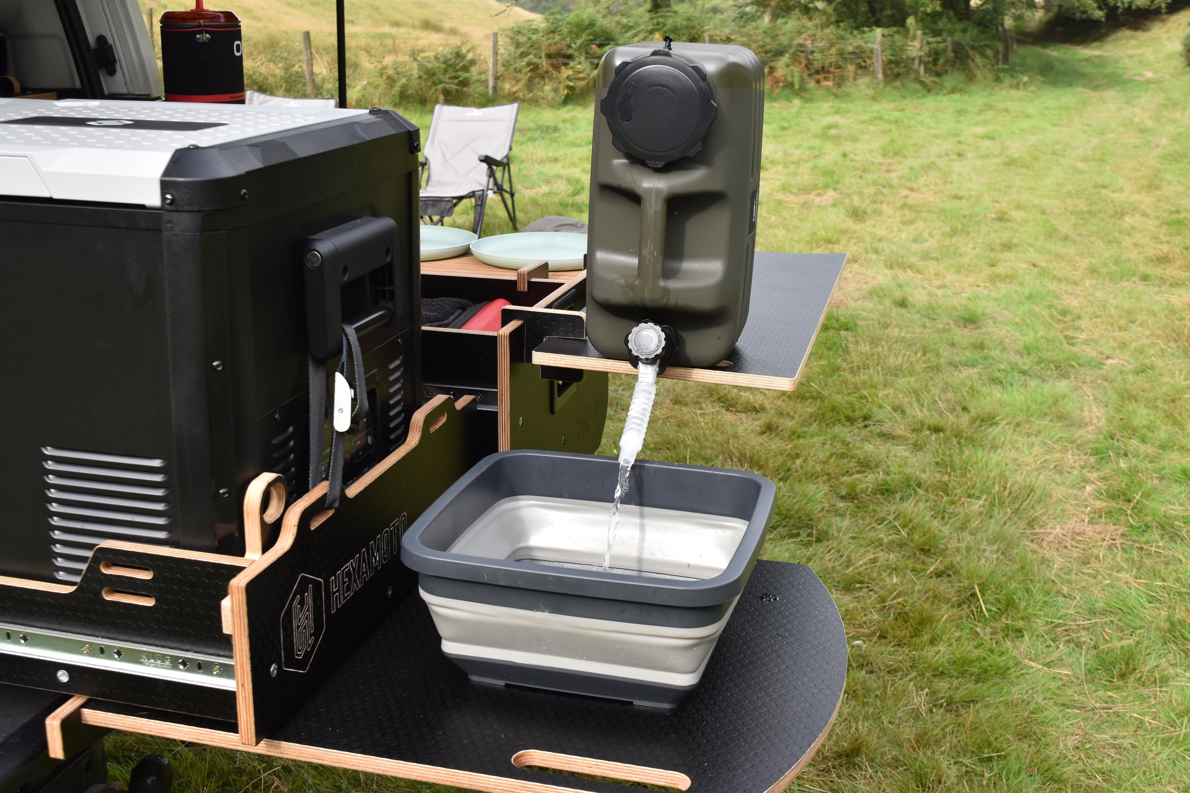 Portable water container system being used outdoors on a Hexamoto Country camping setup.