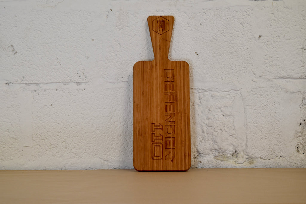 Wooden chopping board with engraved Defender 110 logo on a white brick wall background