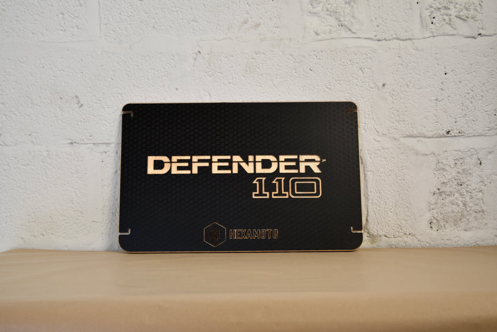 Black table with 'DEFENDER 110' branding on a light wooden surface and white brick wall background.