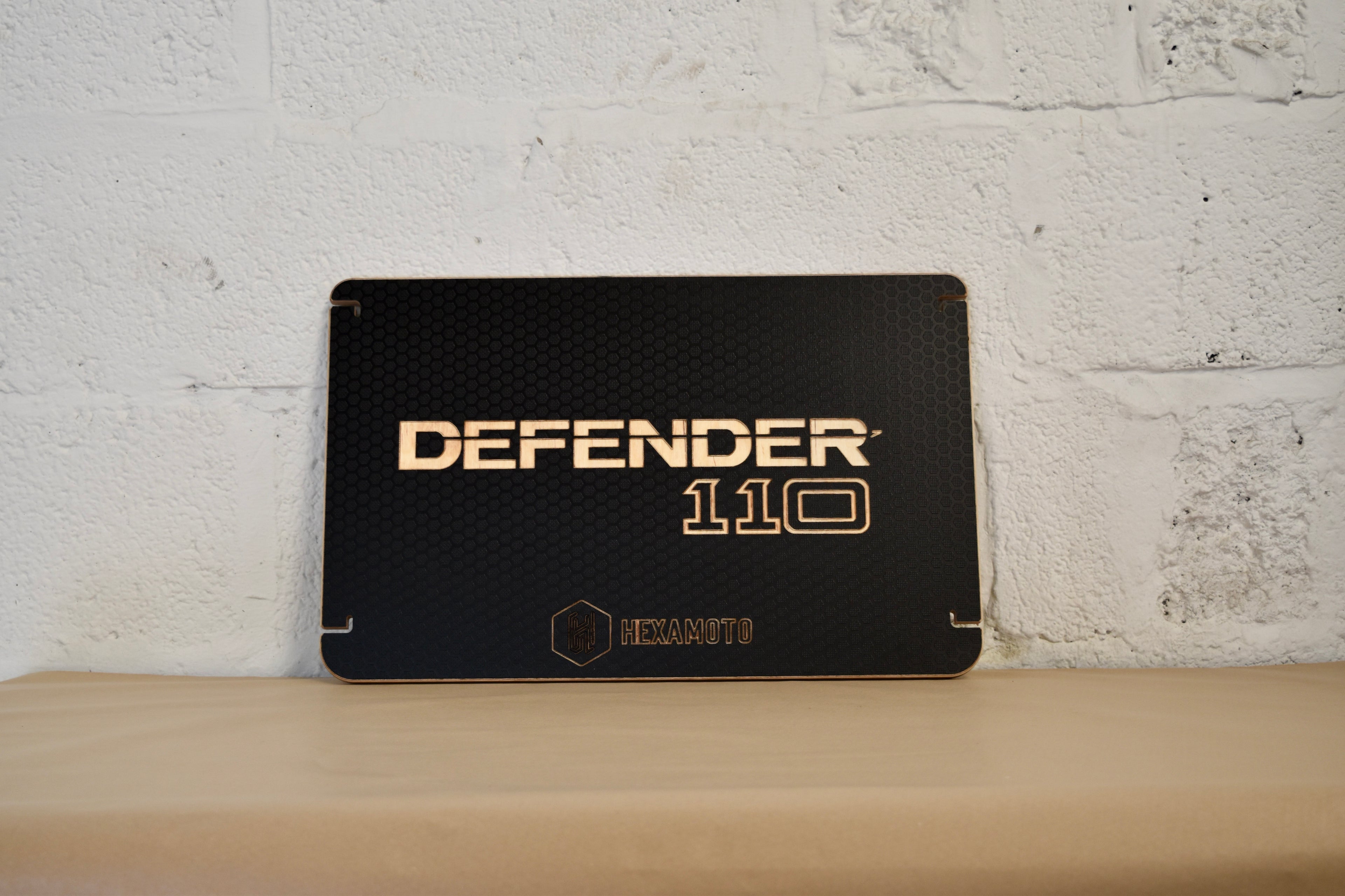 Black table with 'DEFENDER 110' branding on a light wooden surface and white brick wall background.