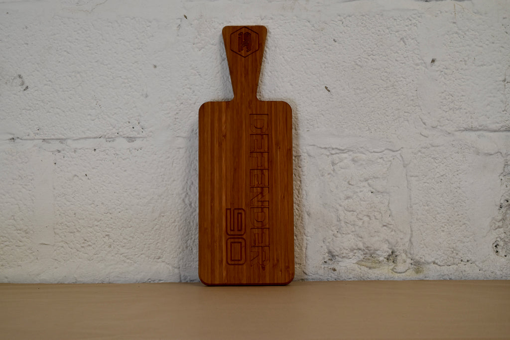 Wooden chopping board with engraved Defender 90 logo on a white brick wall background