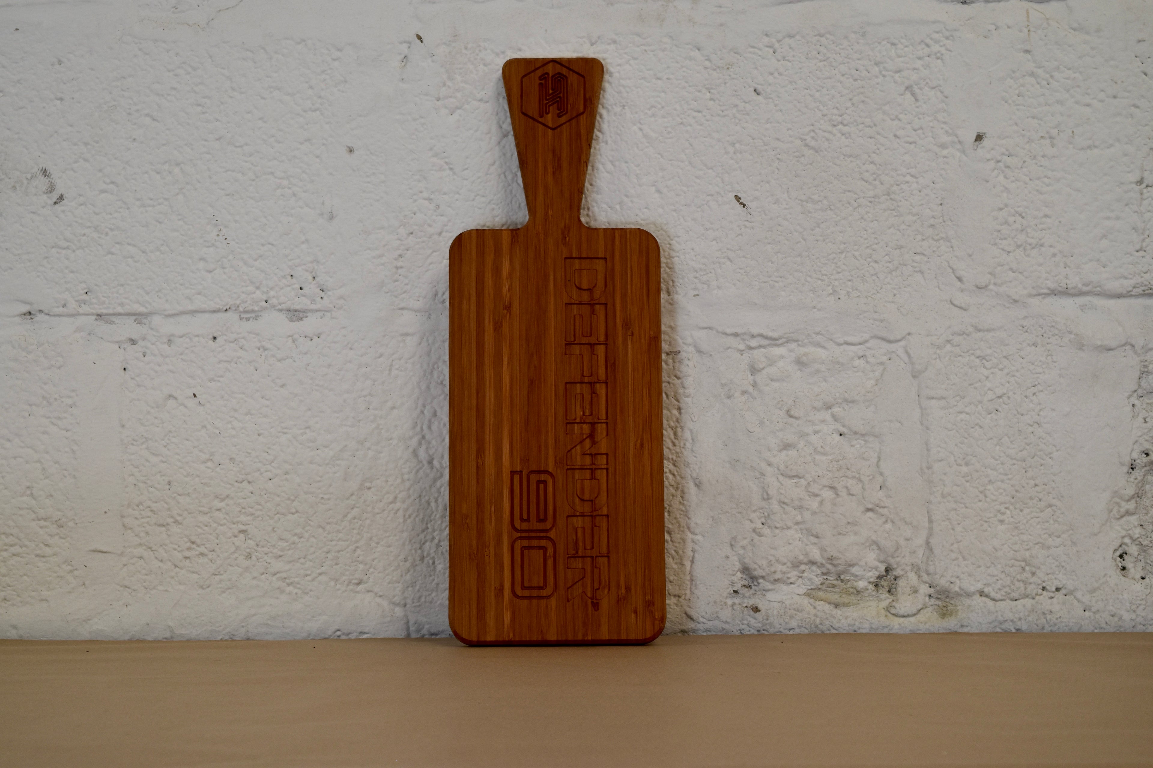 Wooden chopping board with engraved Defender 90 logo on a white brick wall background