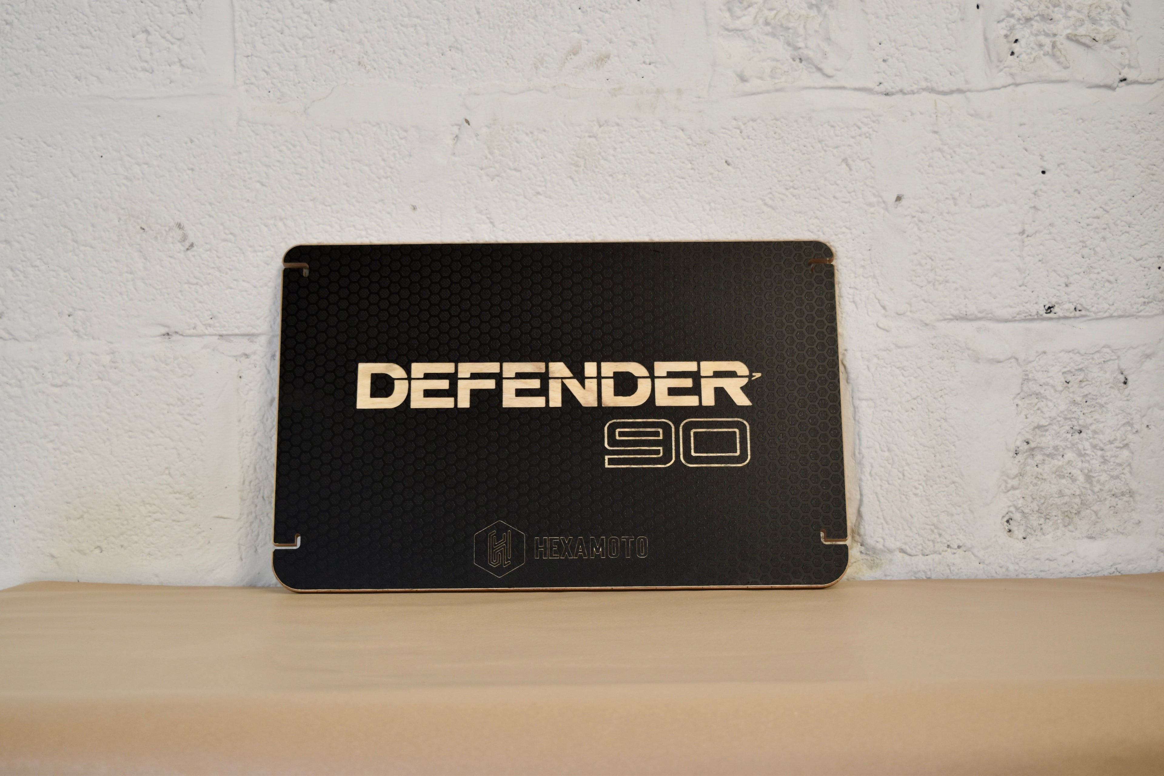 Black table with Defender 90 logo engraving, on a white brick wall background 