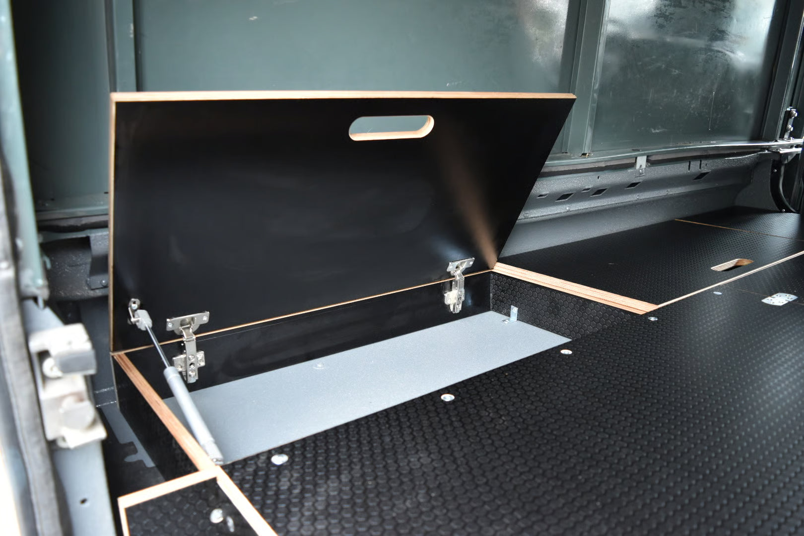 Open storage compartment in a vehicle with a black lid and gas strut to keep it up