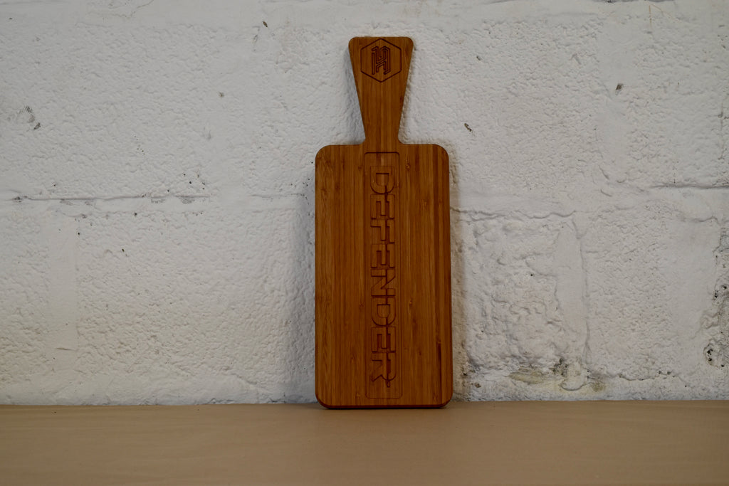 Bamboo chopping board with Defender logo engraved, on a white brick background