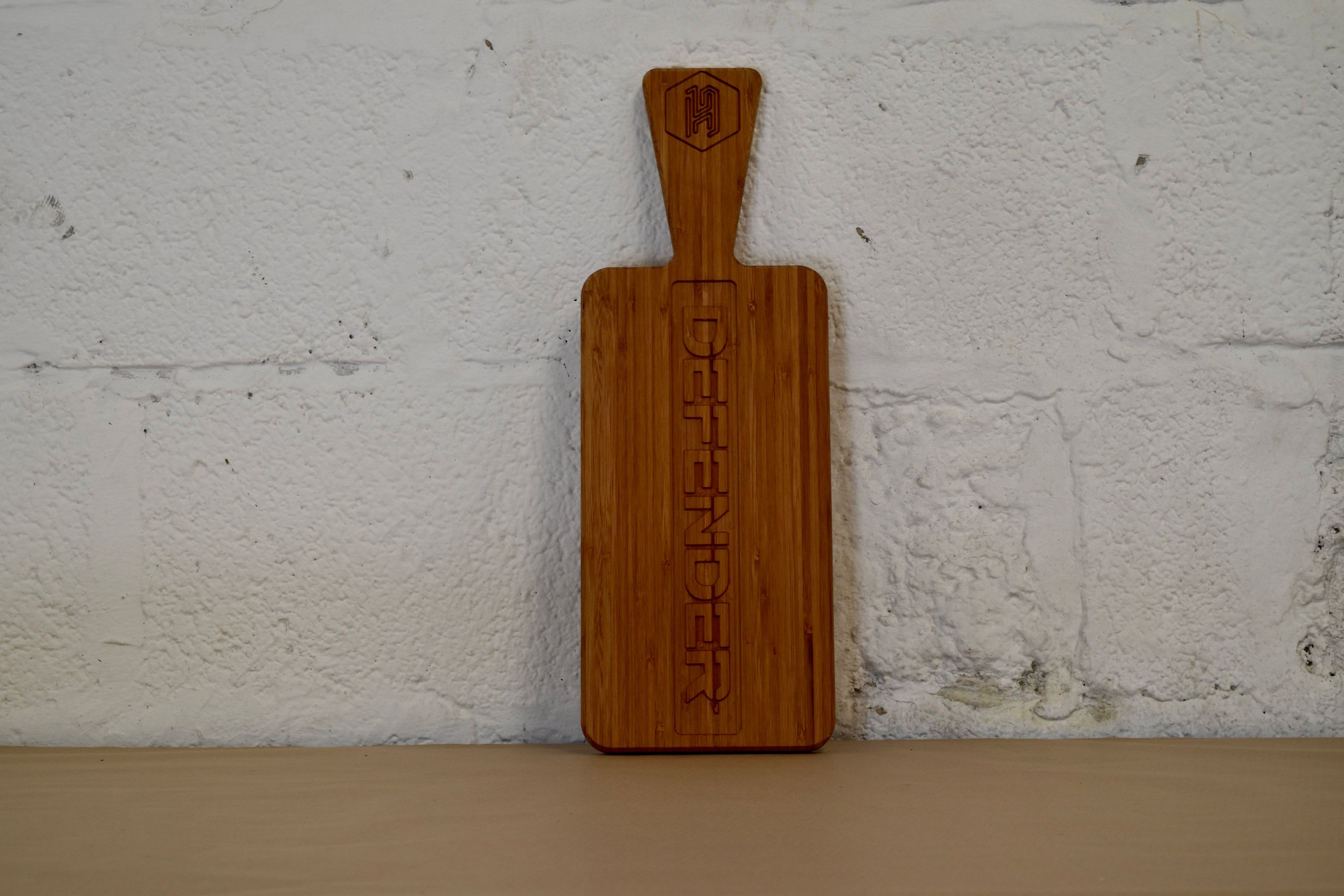 Bamboo chopping board with Defender logo engraved, on a white brick background