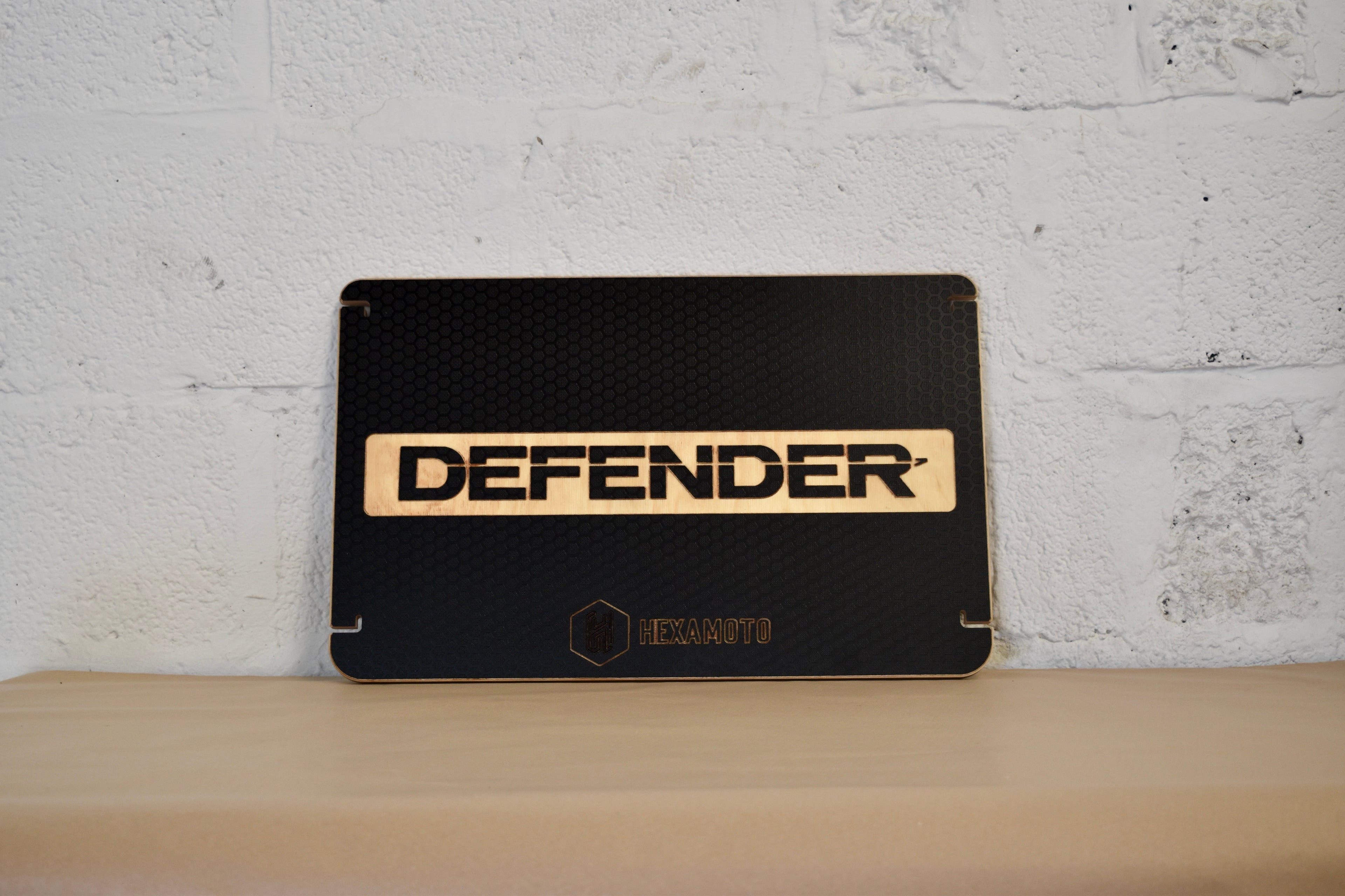 Black table with 'DEFENDER' branding against a white brick wall.