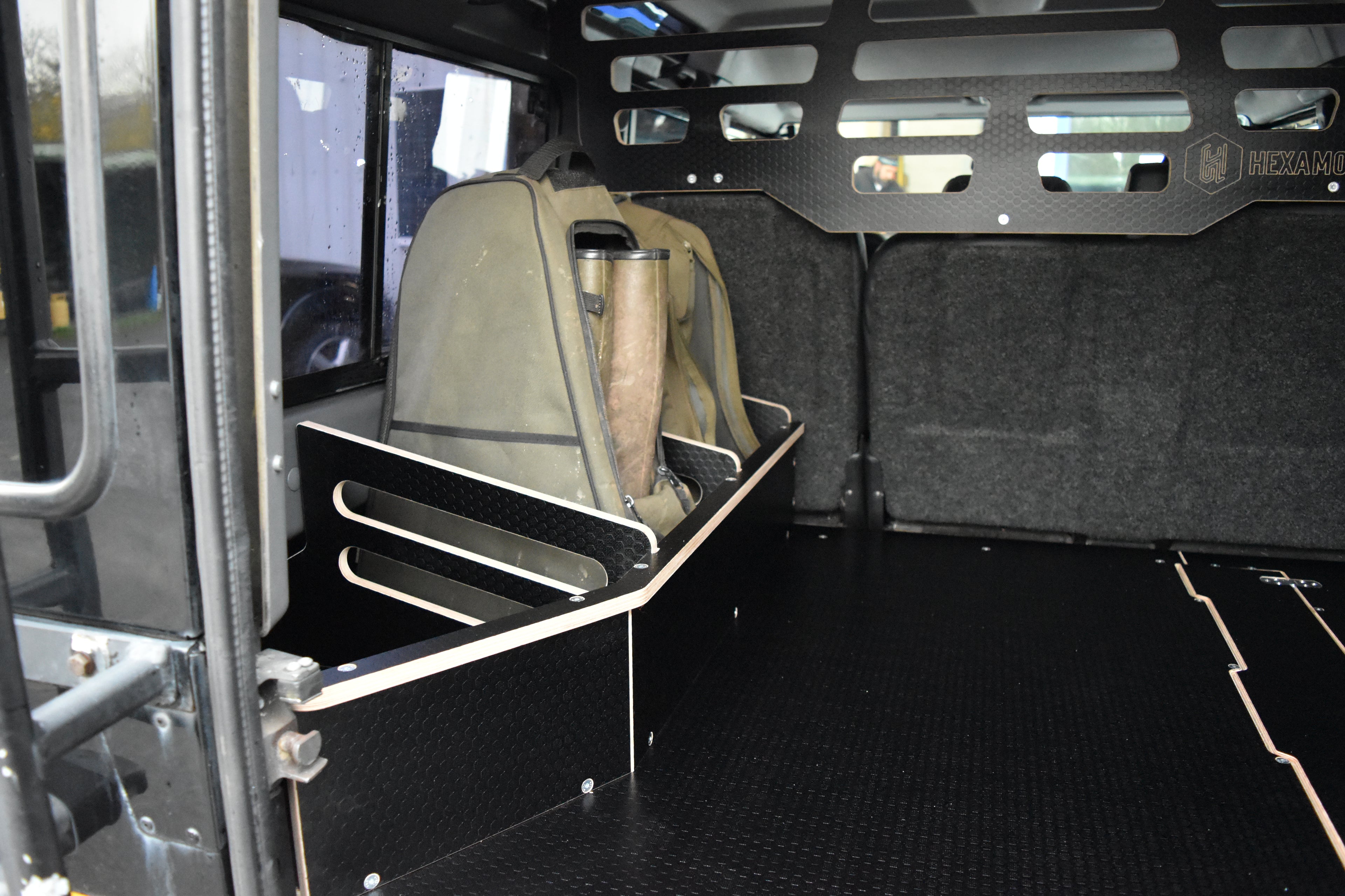 Rear of a Land Rover Defender with a storage basket storing welly boots in bags