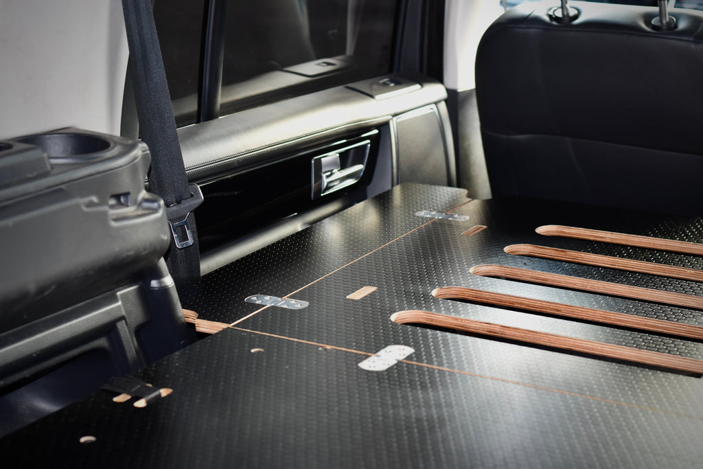 Car interior with folded wooden bed and black seat covers