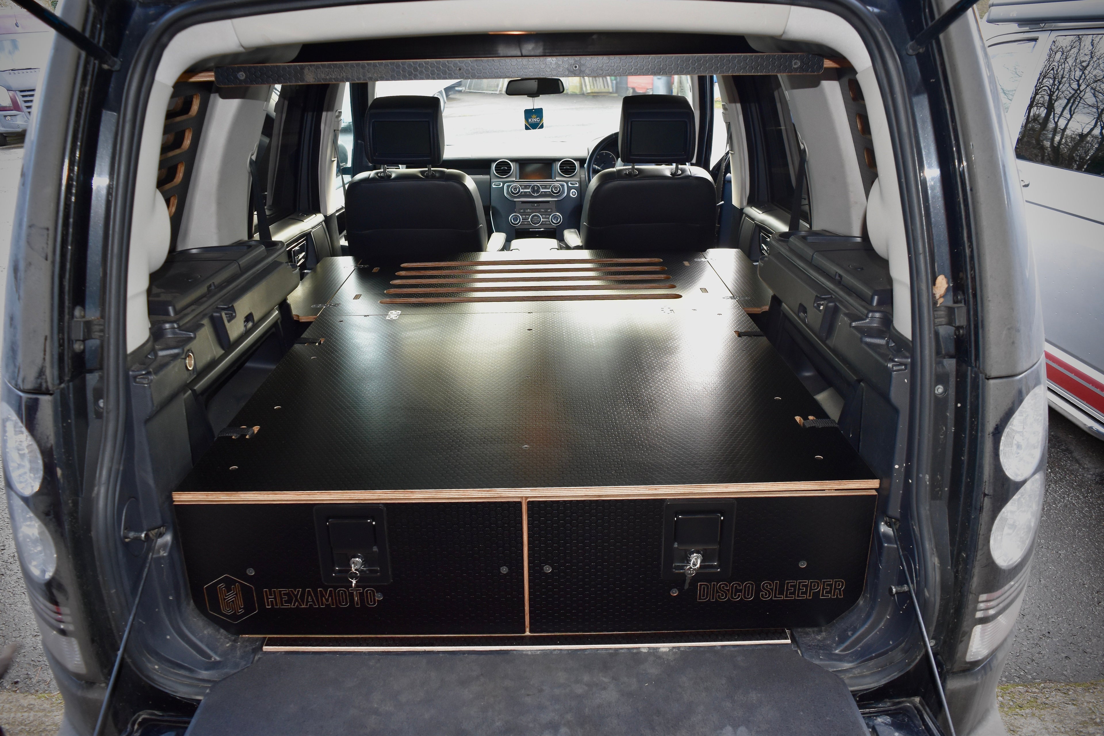Car interior with a flat bed setup and 'Disco Sleeper' branding, for sleeping in a Discovery 3 or 4