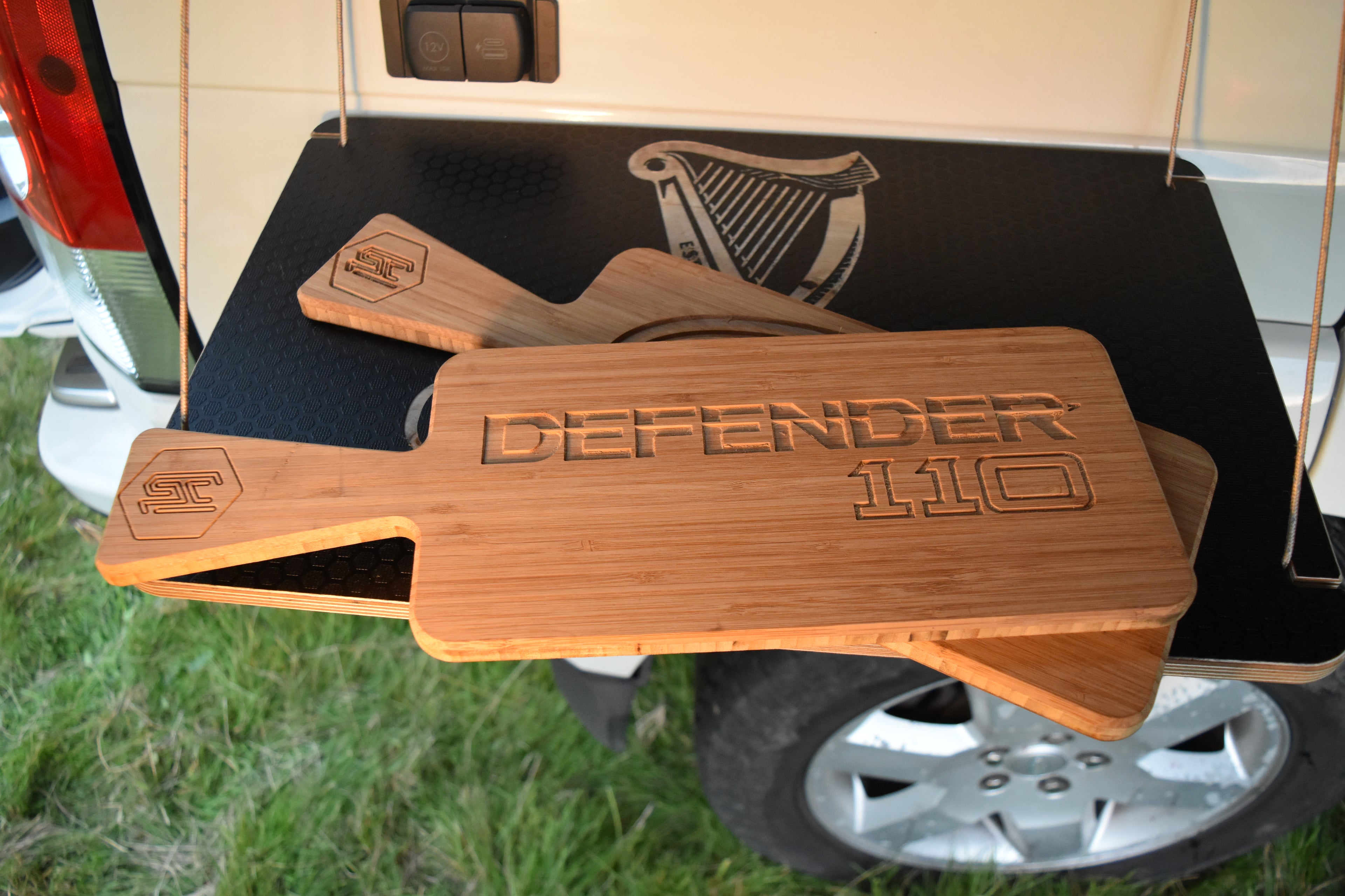 Wooden chopping board with 'Defender 110' engraving on a vehicle's hanging table from Hexamoto