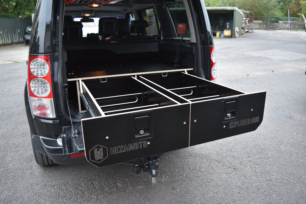 Black storage system attached to the back of a vehicle on a paved surface.