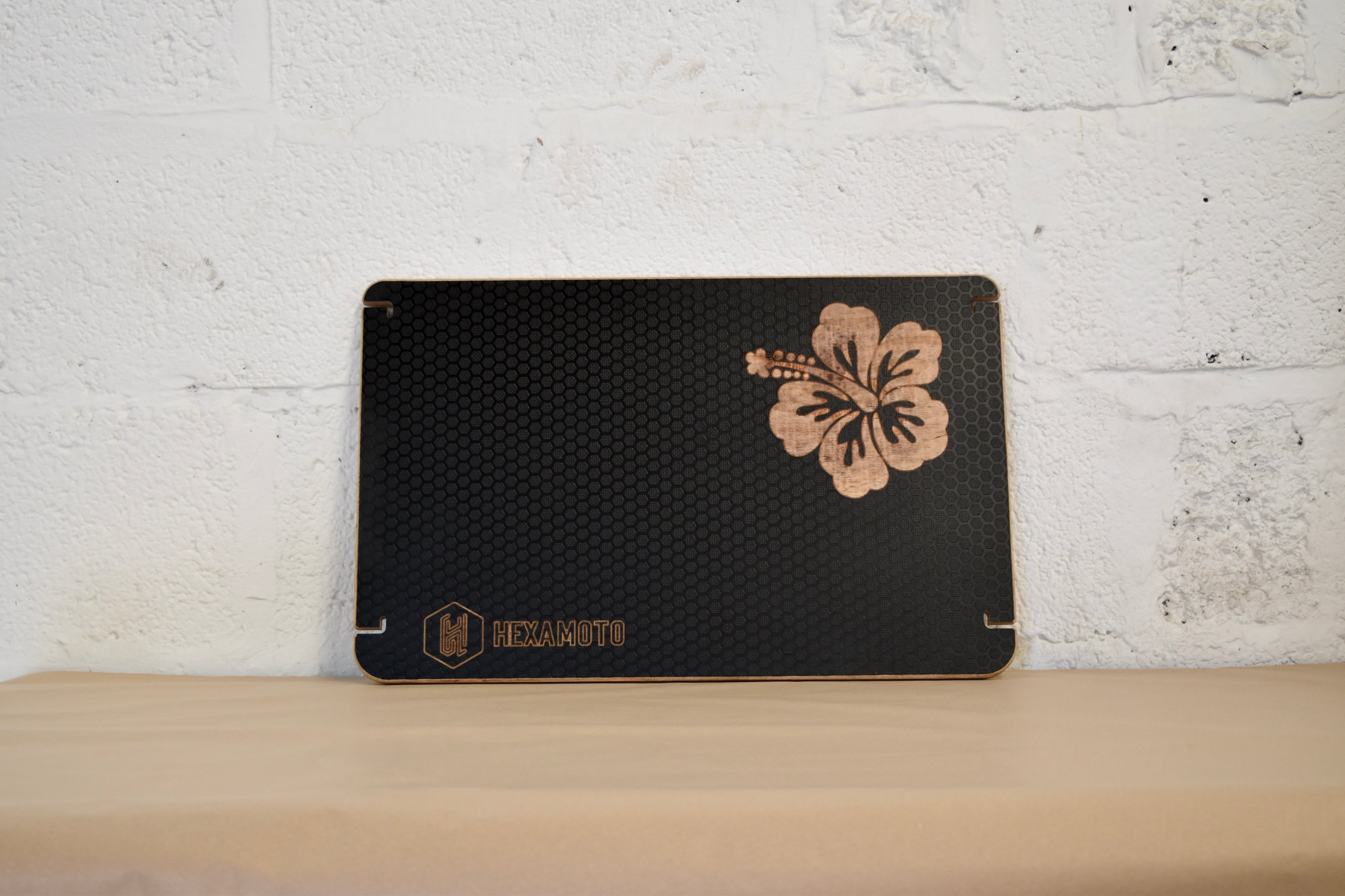 Black table with a floral design and brand name on a wooden surface and white brick wall background