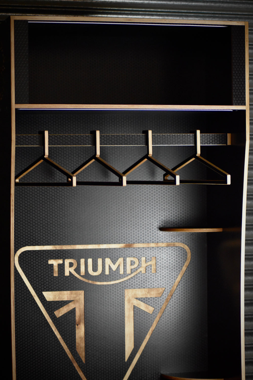 Clothing rack with hangers against a black background featuring the Triumph logo.