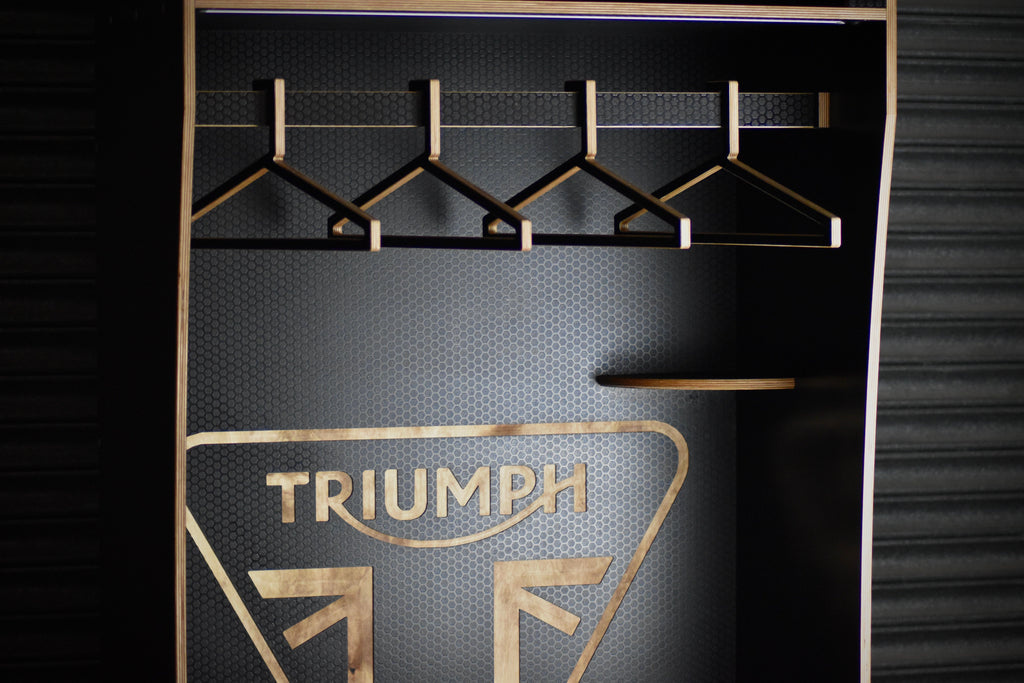 Motorcycle apparel rack with hangers and Triumph logo on a dark background