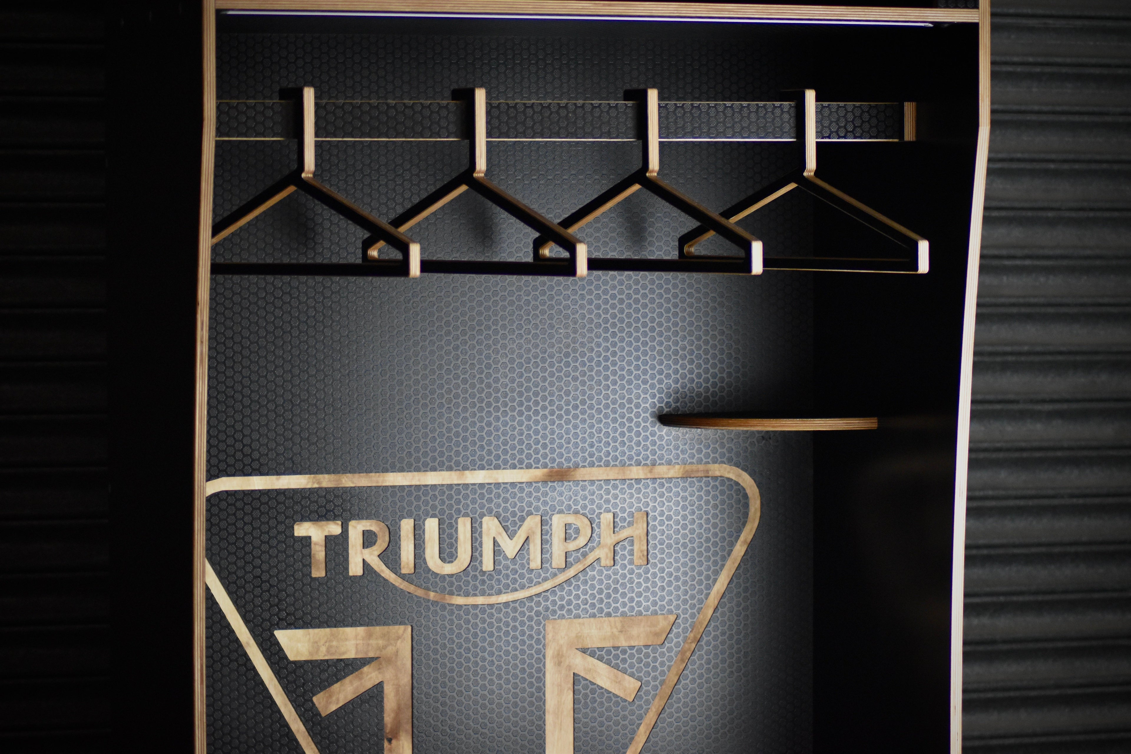 Motorcycle apparel rack with hangers and Triumph logo on a dark background