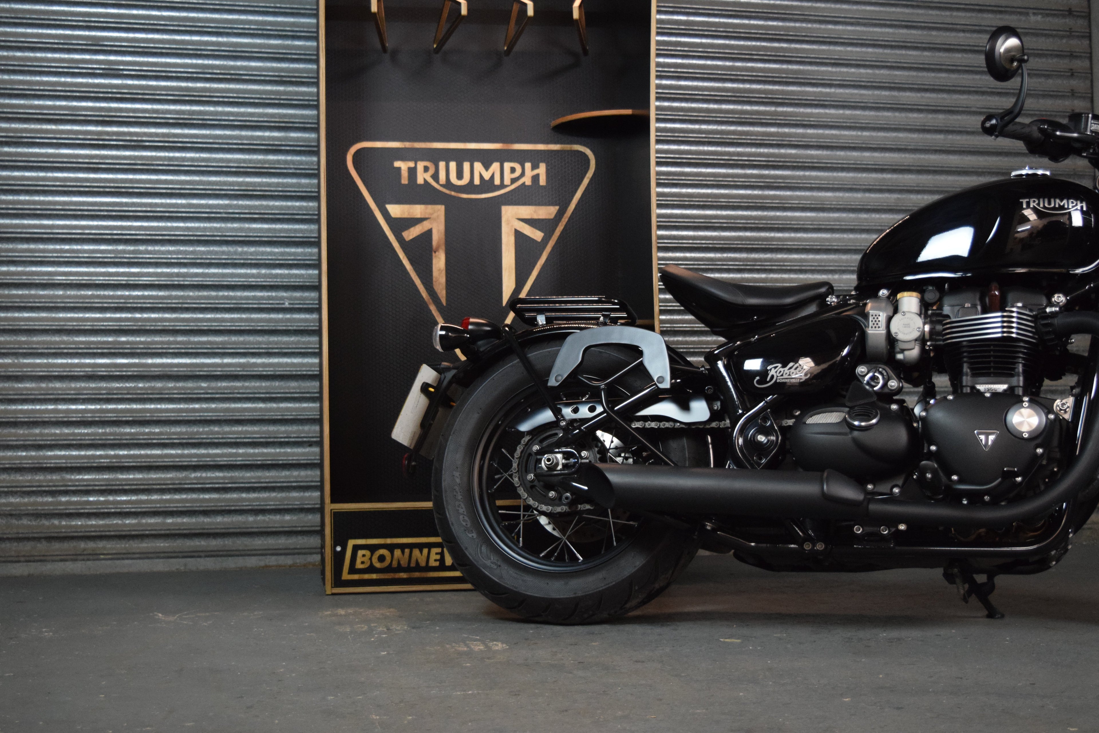 Black Triumph motorcycle parked in front of a garage door with a storage system in the background sporting a Triumph logo.