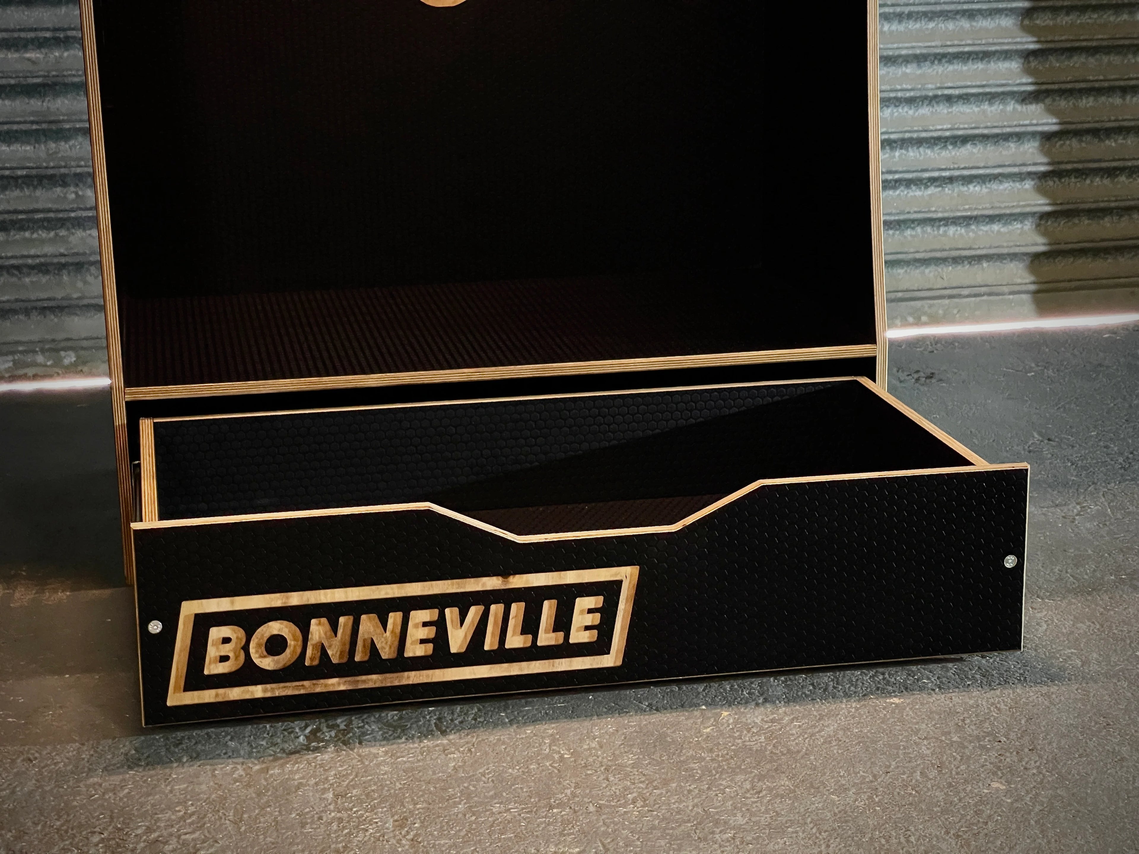 Black wooden storage box on a concrete floor with metal shutter background and 'Bonneville' logo