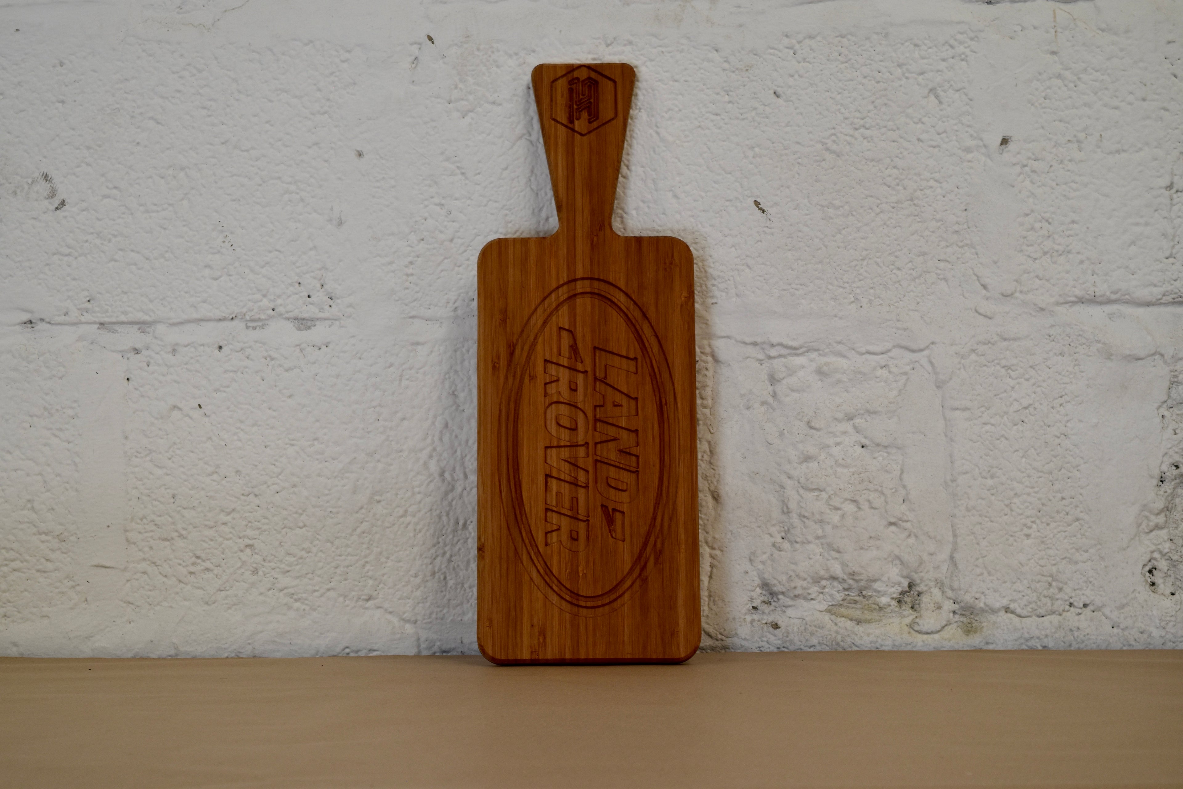 Wooden chopping board with engraved Land Rover logo on a white brick wall background