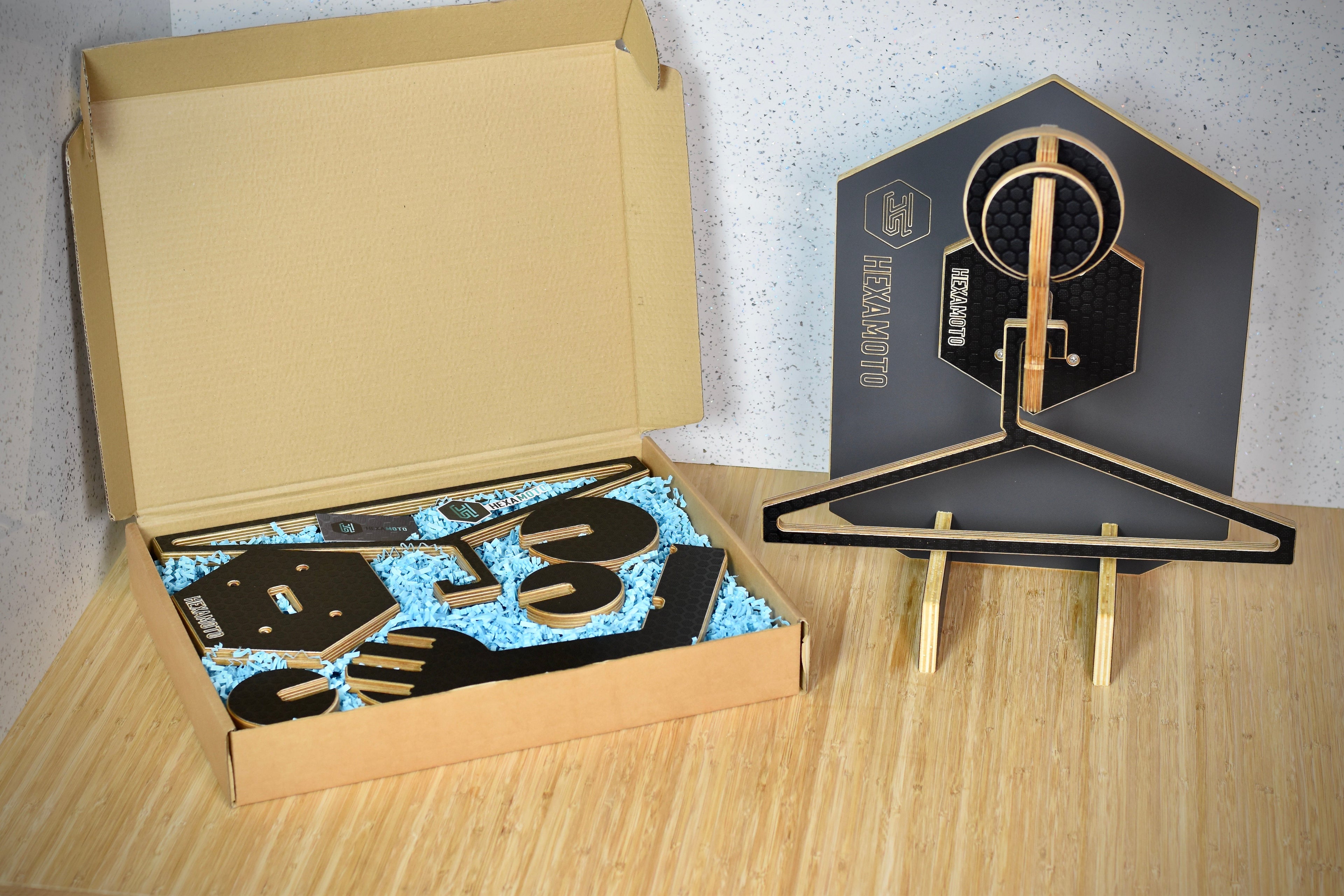 Wooden system with geometric design next to an open cardboard box on a wooden surface with the Hexamoto Mini items inside