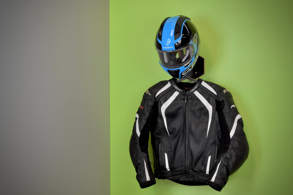 Black motorcycle jacket and helmet on a green background, hanging from a Hexamoto Mini