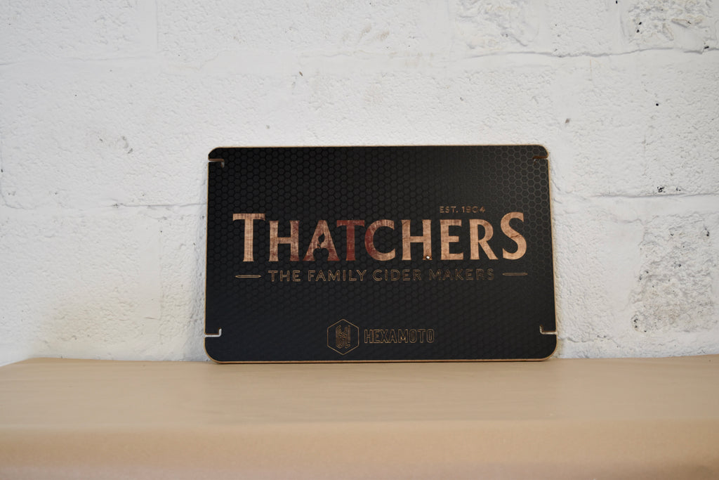 Wooden table with Thatchers logo engraved on a white brick background