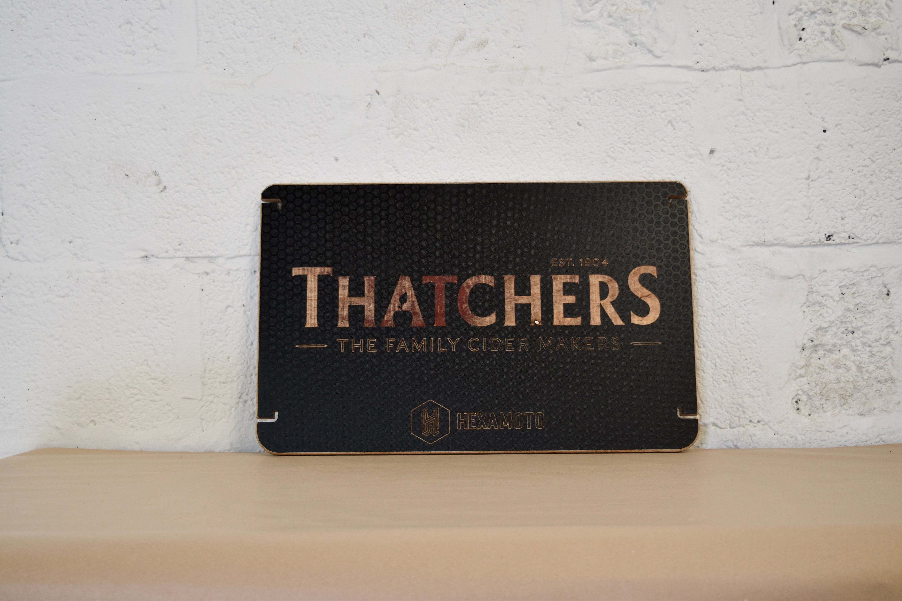 Wooden table with Thatchers logo engraved on a white brick background