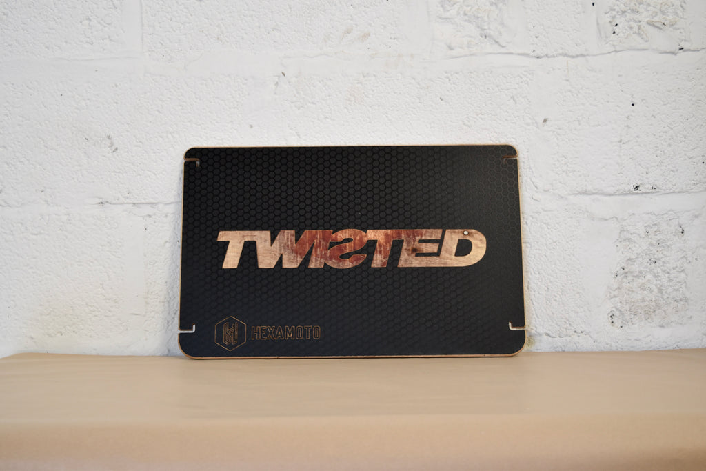 Black textured table with 'TWISTED' branding on a white brick wall background