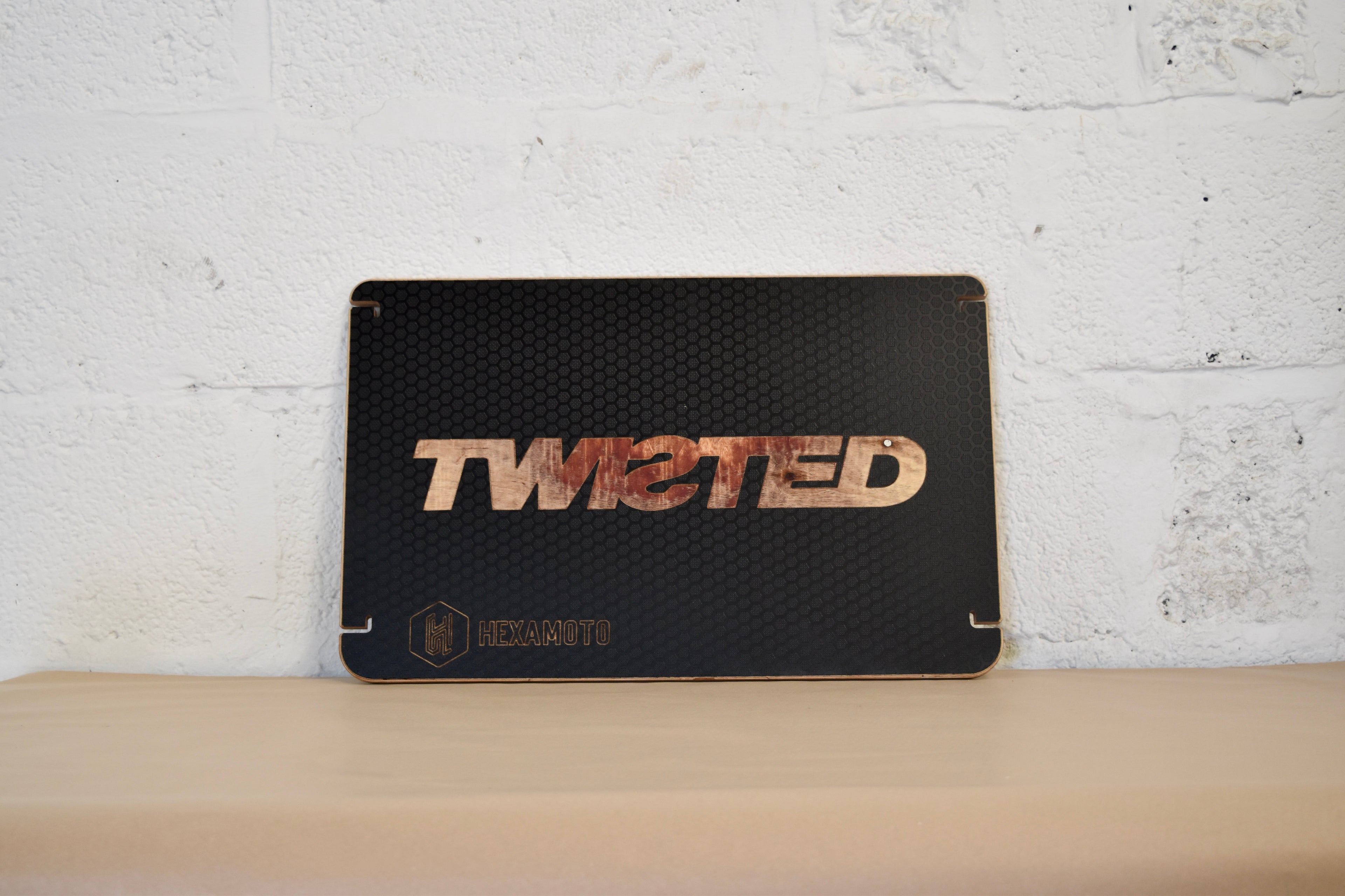 Black textured table with 'TWISTED' branding on a white brick wall background