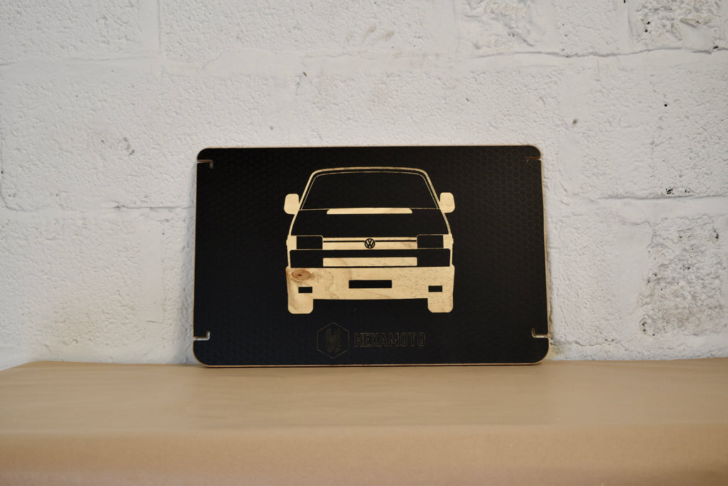 Black table with car silhouette engraved on a wooden surface against a white brick wall.