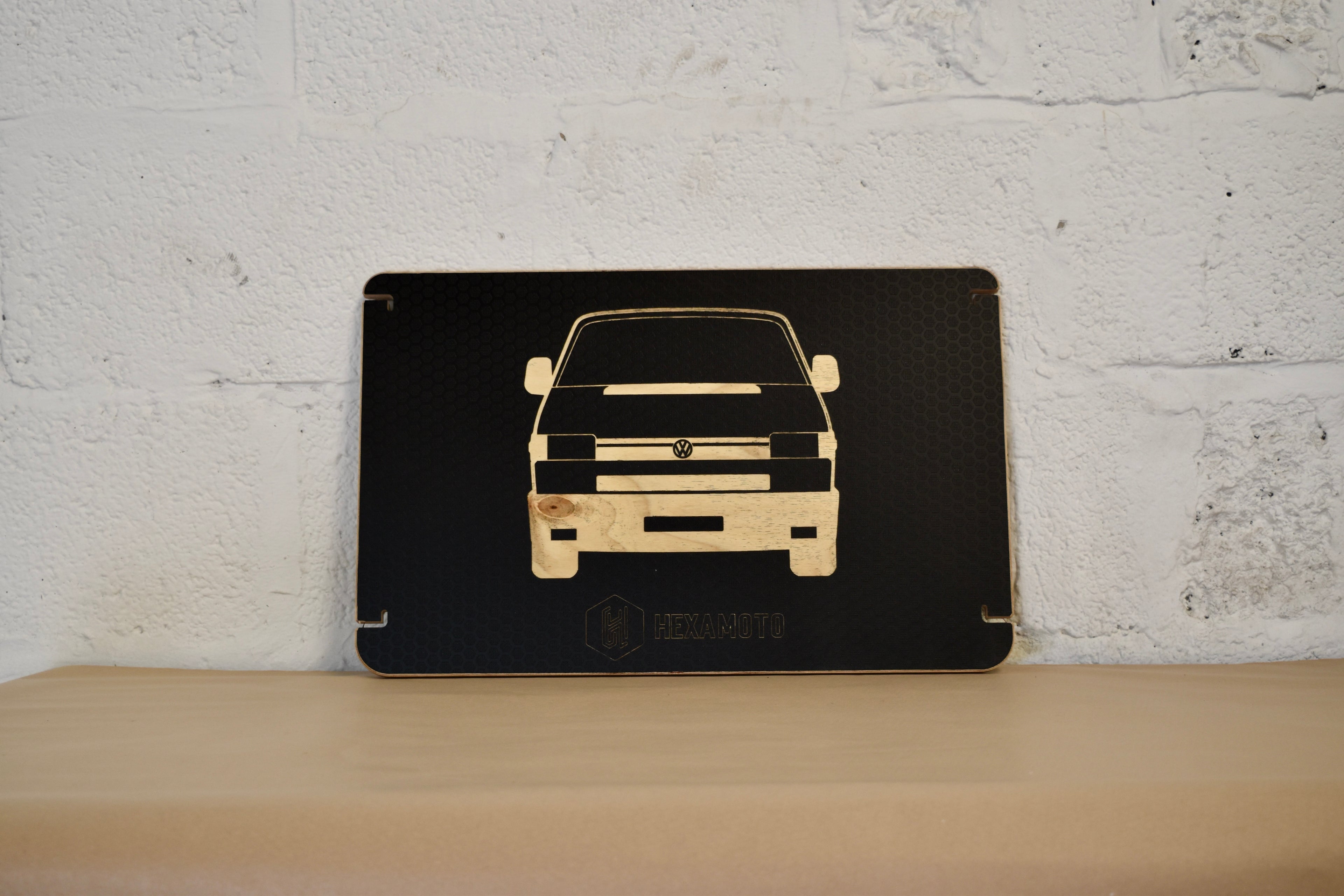 Black table with car silhouette engraved on a wooden surface against a white brick wall.