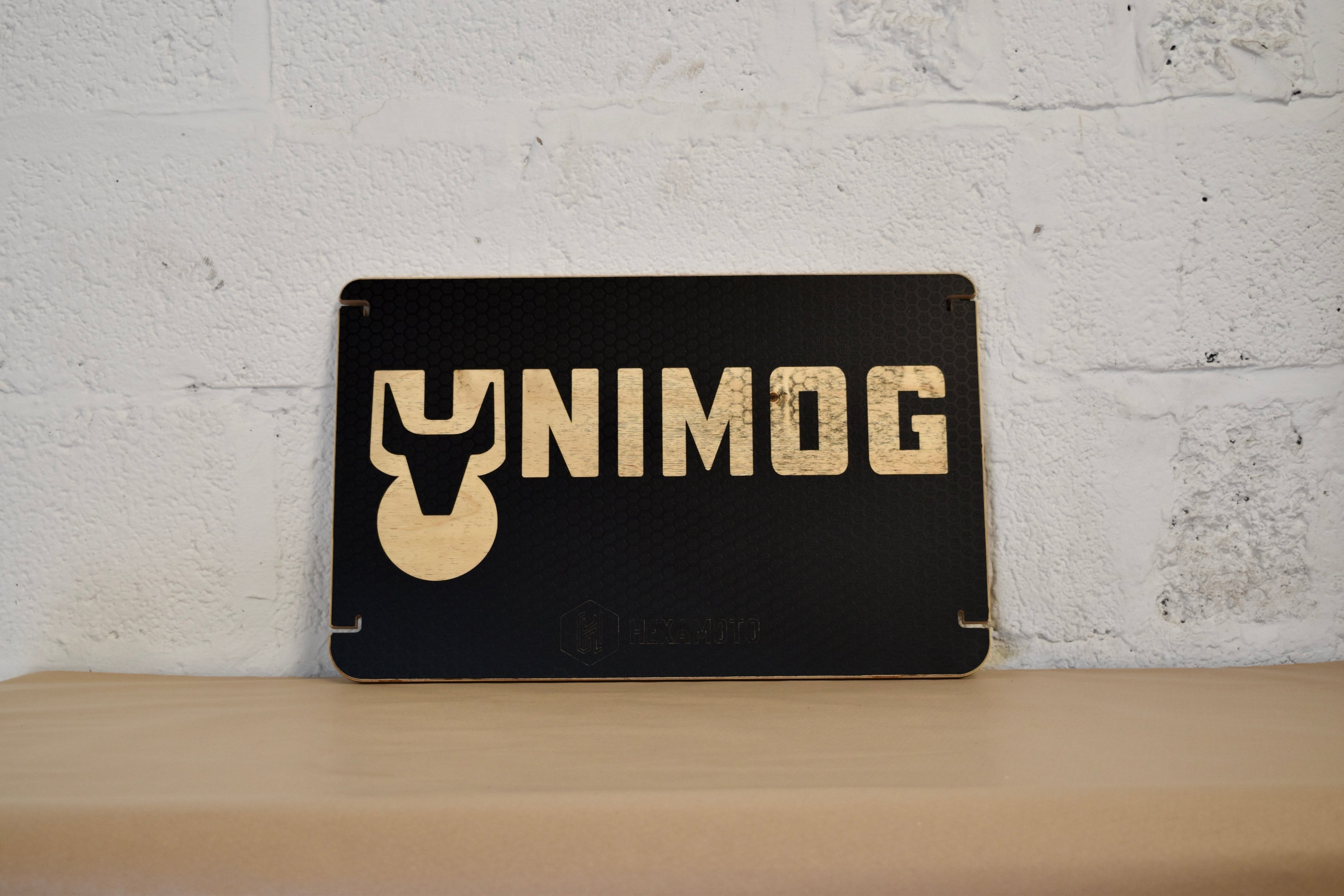 Black table with 'UNIMOG' logo on a wooden surface against a white brick wall.