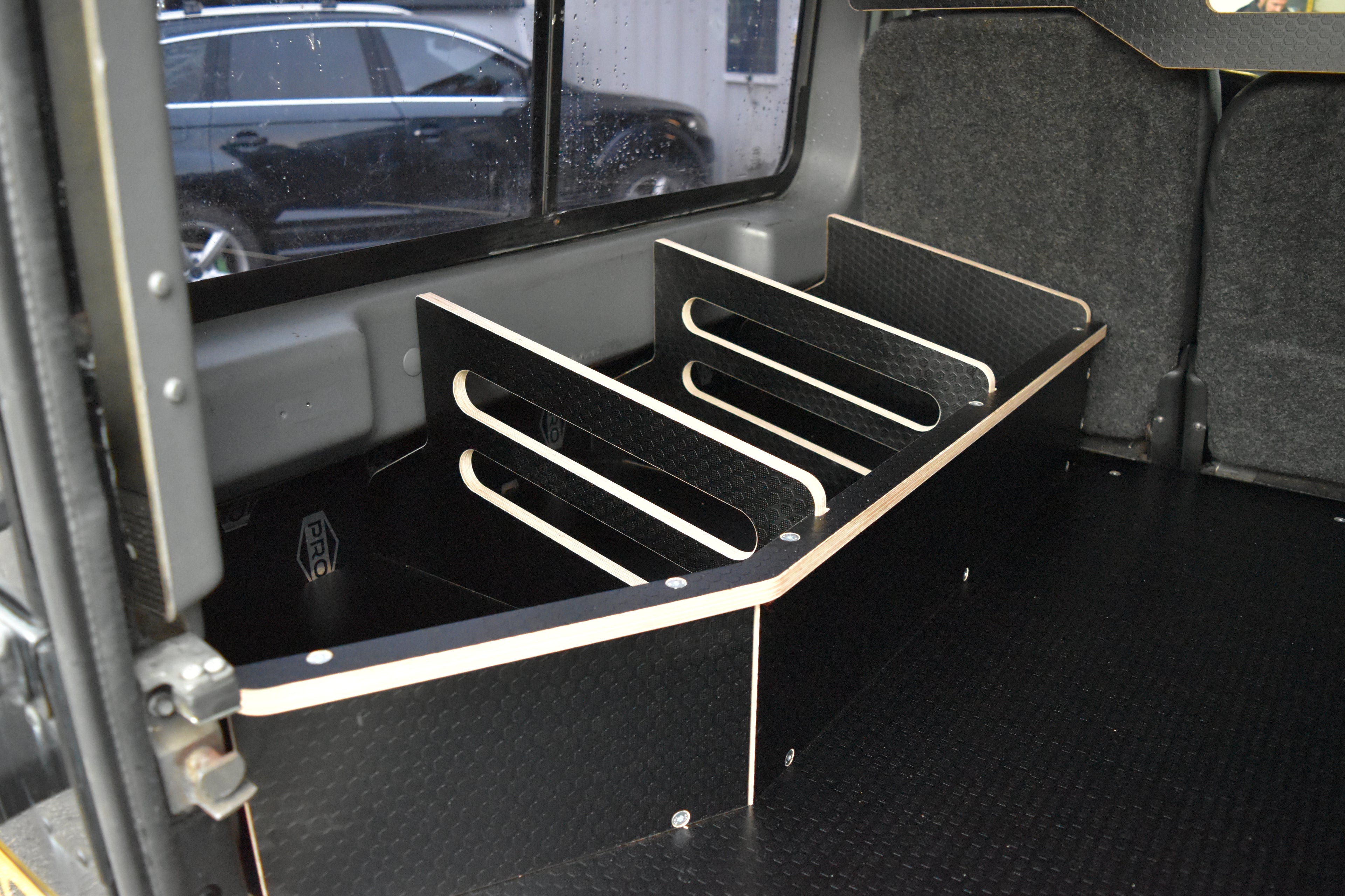 Black wooden storage system in back of a Land Rover Defender, including the Hexamoto Utility Storage Basket