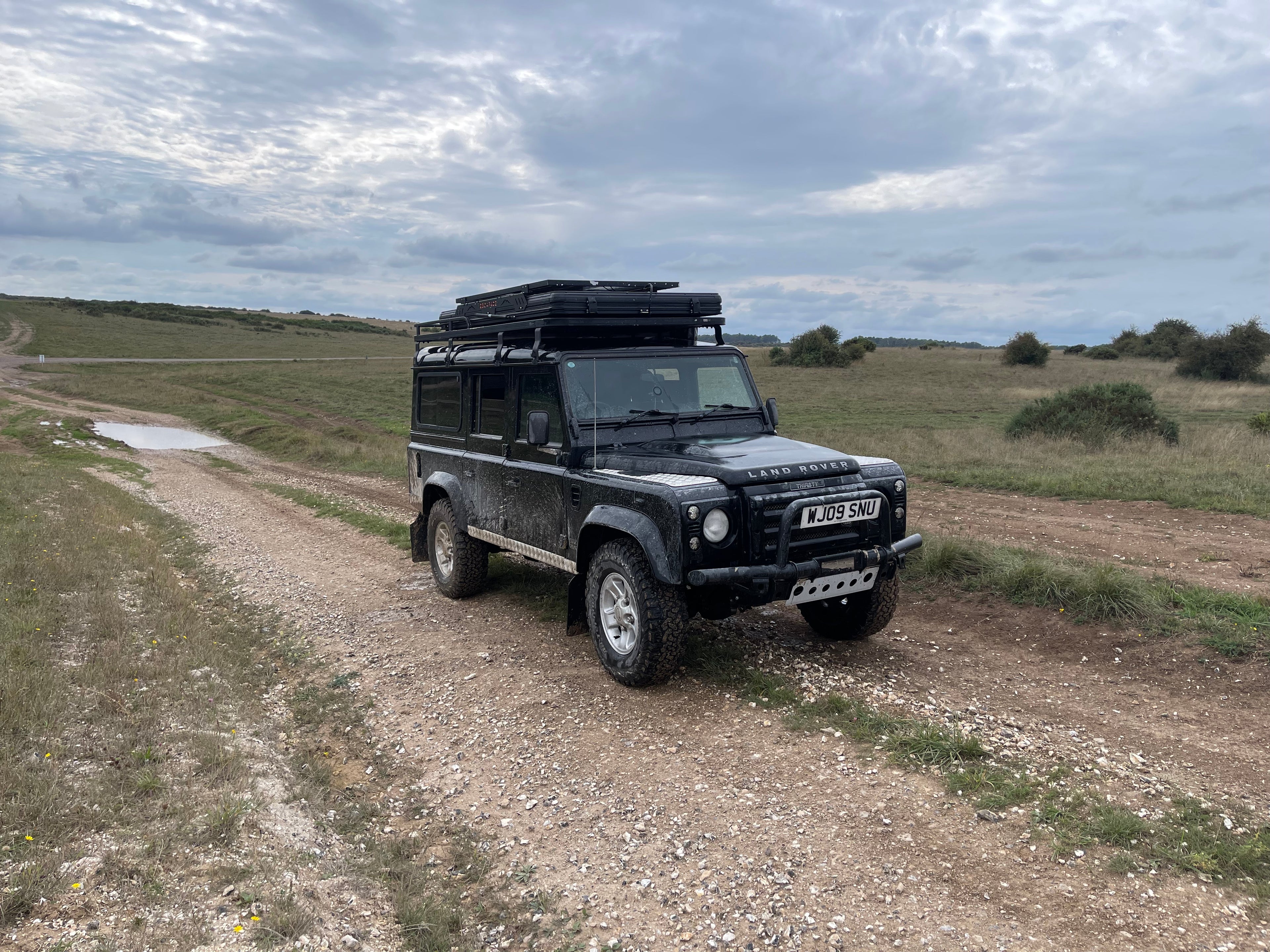 Black Land Rover Defender on a dirt road with a cloudy sky