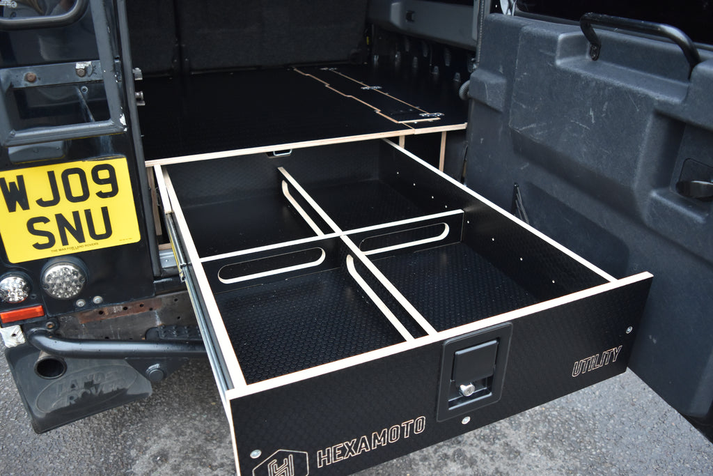 Black storage drawer with metal handles on a vehicle, branded 'Hexamoto'.