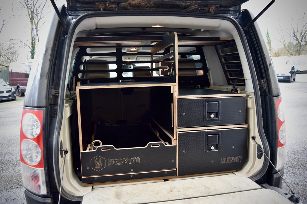 Land Rover Discovery 4 interior with storage compartments labeled 'Hexamoto', in a parking lot.